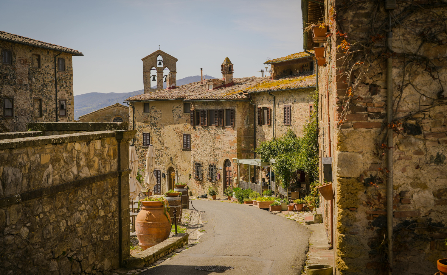 Quiet cobblestone street lined with historic stone buildings in the medieval village of Monteriggioni, Tuscany, Italy.
