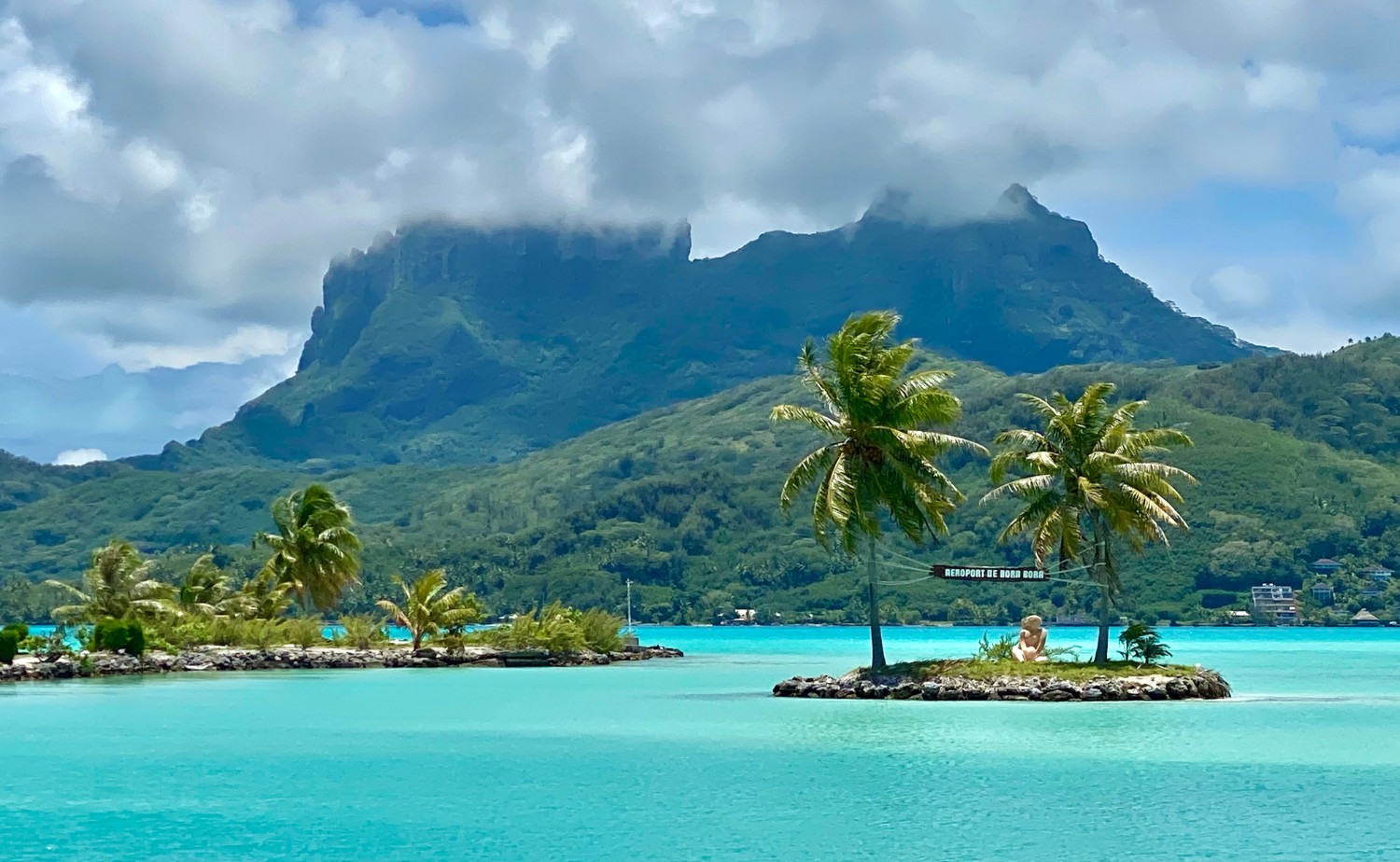 Turquoise lagoon with small palm-covered islets and dramatic mountain peaks in the background in Bora Bora, highlighting the natural beauty of French Polynesia.