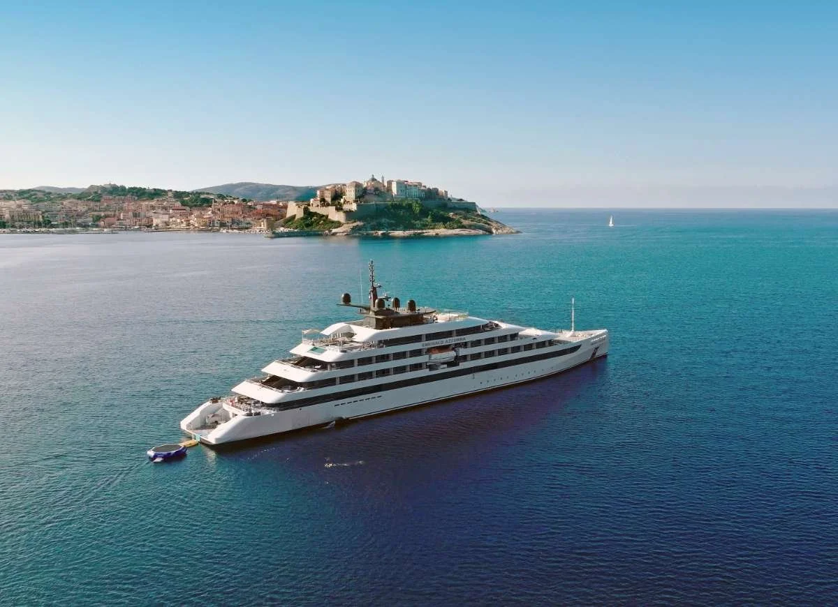 Emerald Cruises luxury yacht sailing through turquoise Mediterranean waters near a historic coastal town.