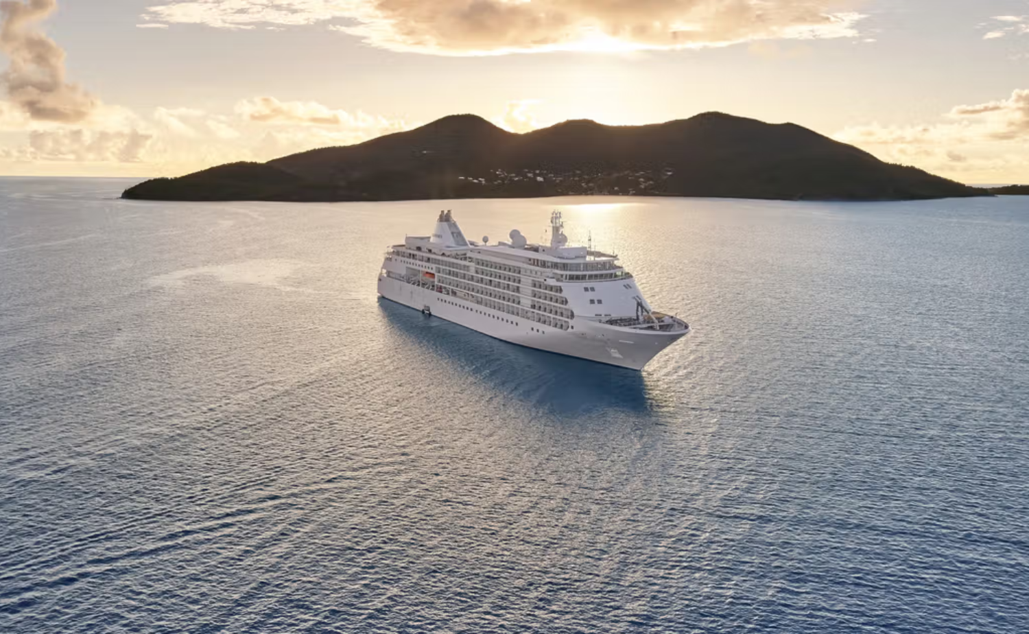 Silversea luxury cruise ship sailing past a Caribbean island at sunset