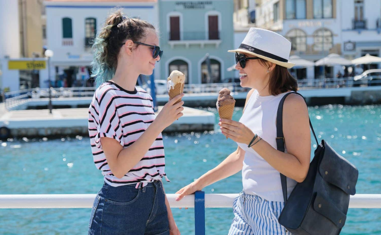 Mother and teenage daughter enjoying gelato while exploring a charming European riverside town