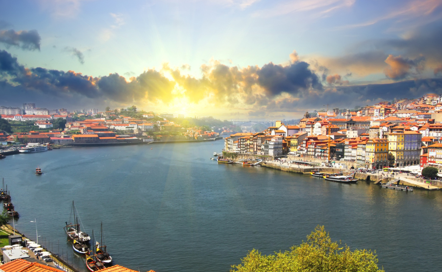 Sunrise over Porto's historic waterfront along the Douro River in northern Portugal with colorful buildings and traditional rabelo boats