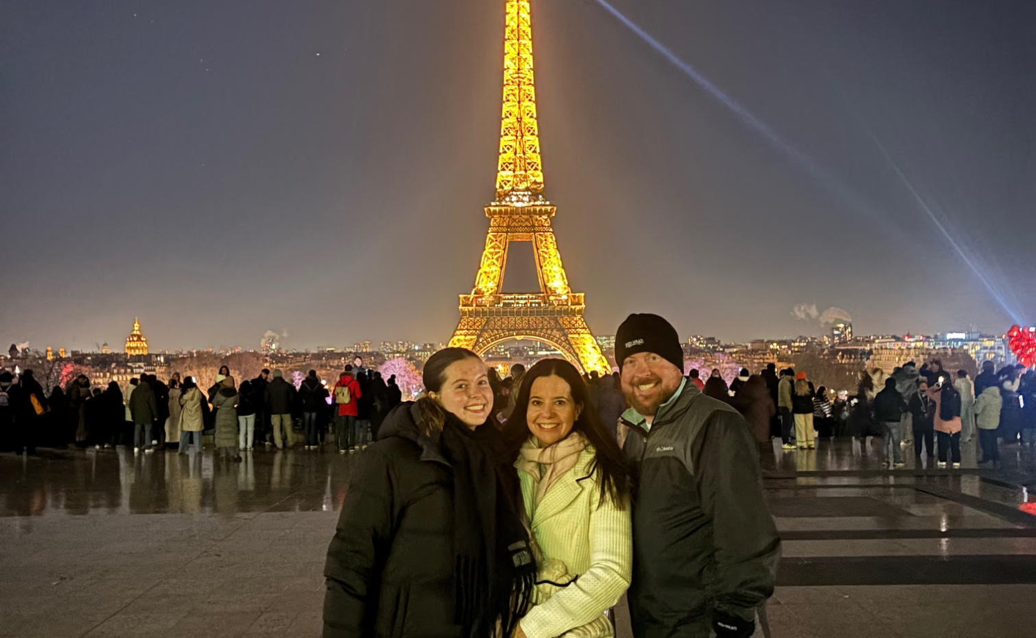 Family standing in front of the illuminated Eiffel Tower at night during a winter visit to Paris.