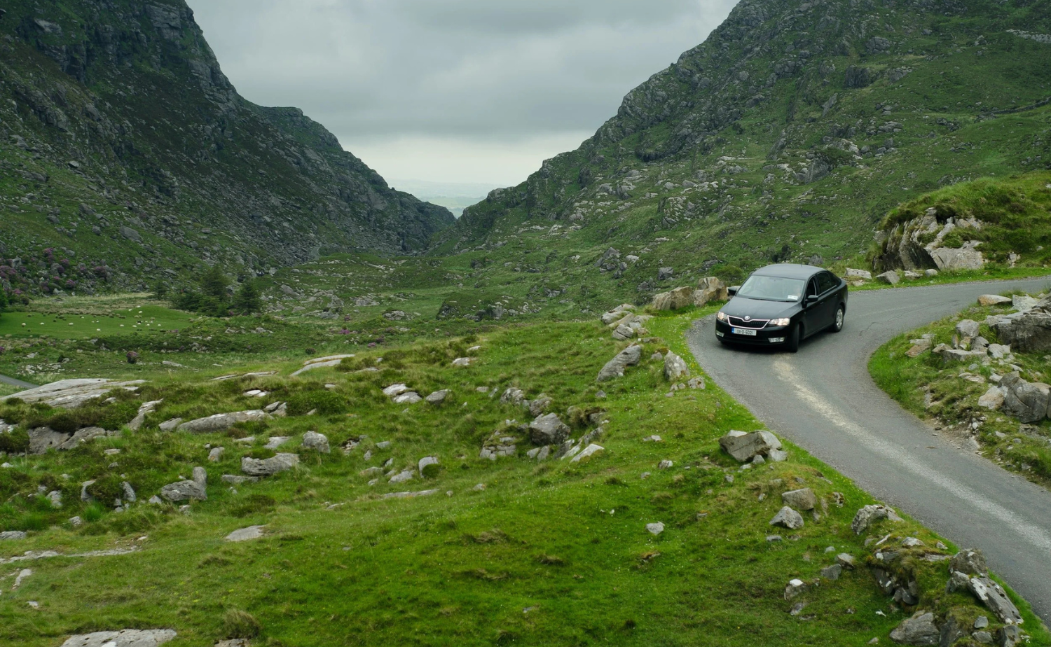 A car driving along a narrow scenic road through a mountain pass in rural Ireland.