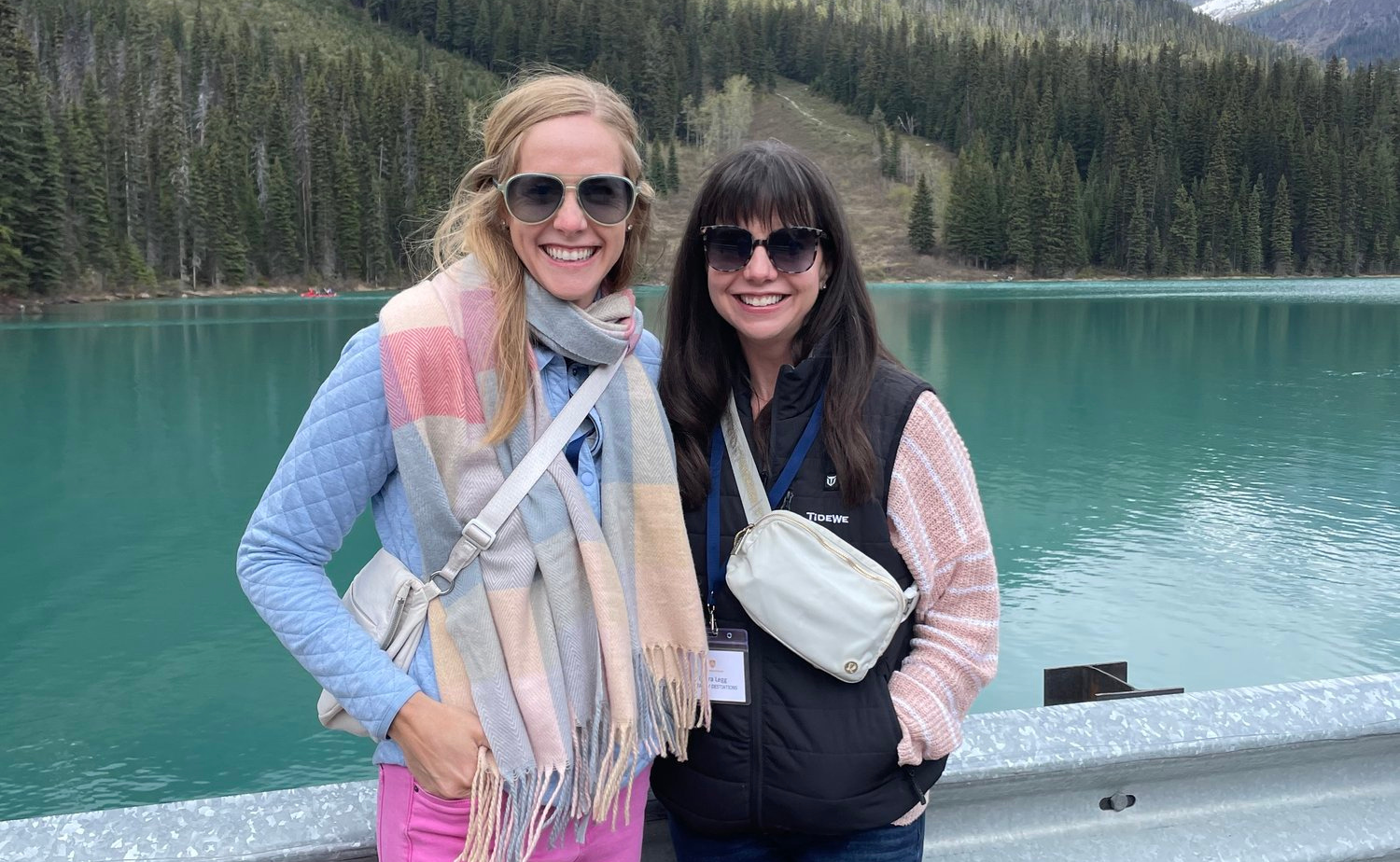 Laura and Molly smiling beside the turquoise waters of Emerald Lake with evergreen trees and mountains in the background.