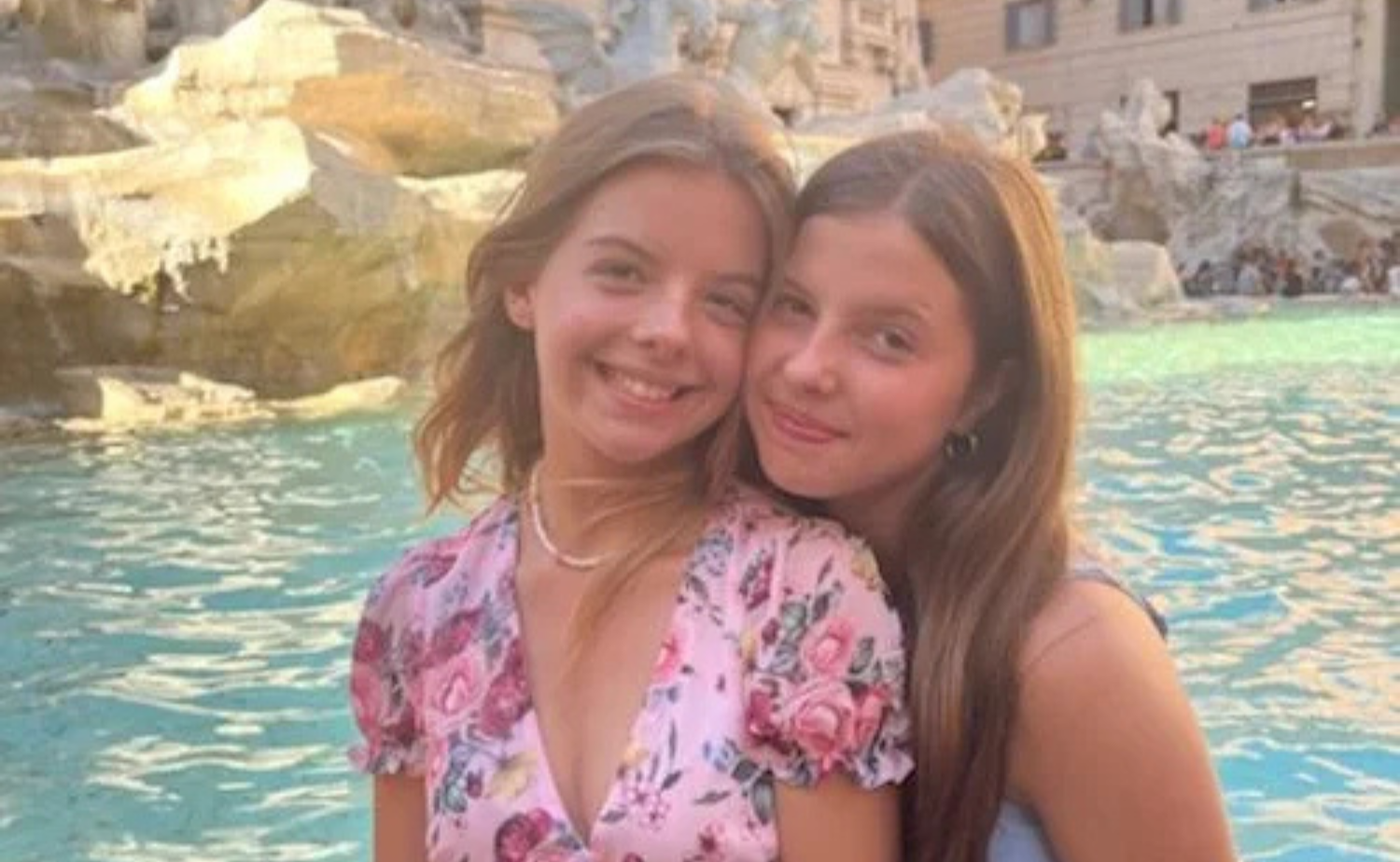 Two girls smiling together in front of the Trevi Fountain in Rome.