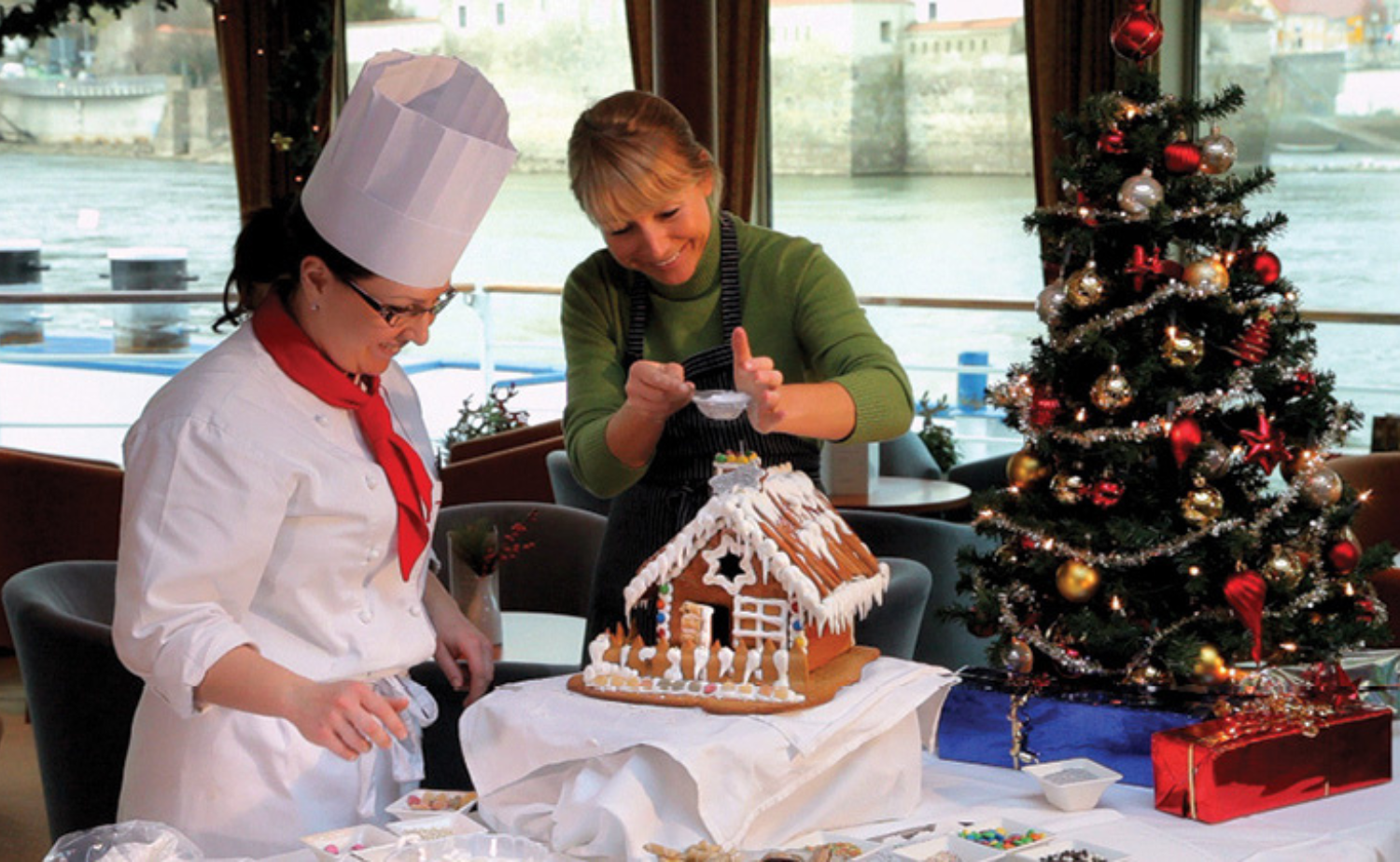 Guests decorating a gingerbread house with a Viking chef beside a Christmas tree during a festive European river cruise