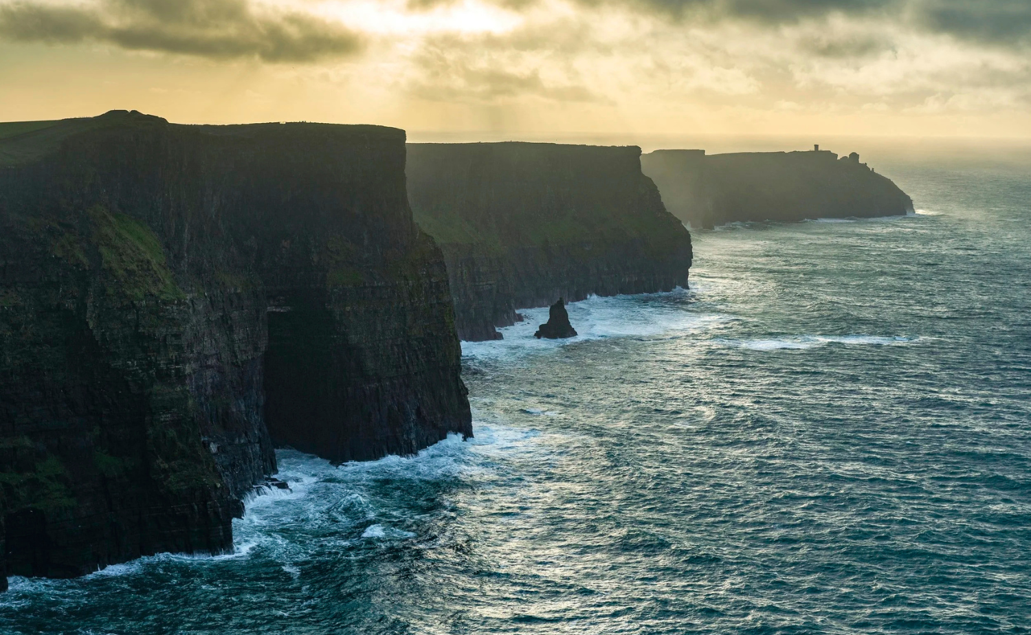 The Cliffs of Moher rising dramatically above the Atlantic Ocean under cloudy skies