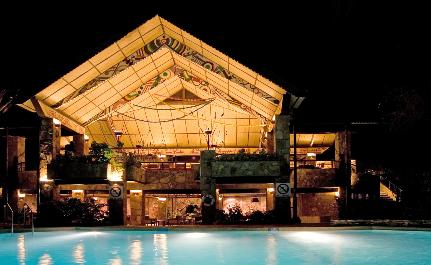 Luxury African safari lodge glowing at night beside a swimming pool.