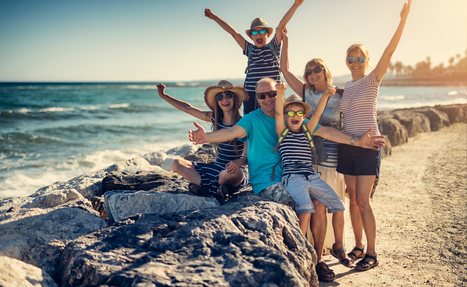 Grandparents and grandchildren smiling together on a sunny beach during a family vacation.