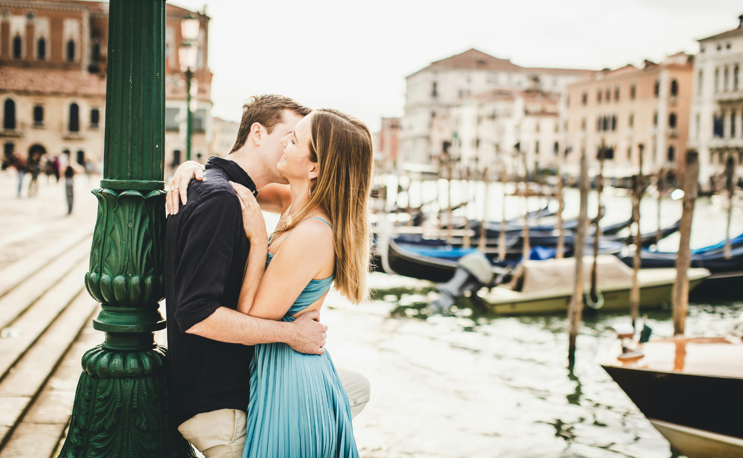 Couple embracing by a lamppost in Venice with gondolas in the background