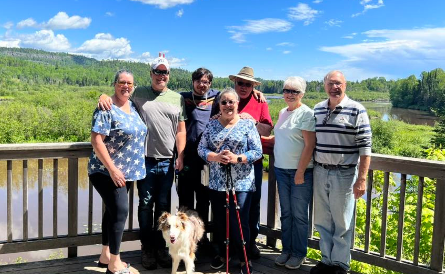 A multi-generational family posing together at a scenic overlook surrounded by trees and water during a summer vacation.