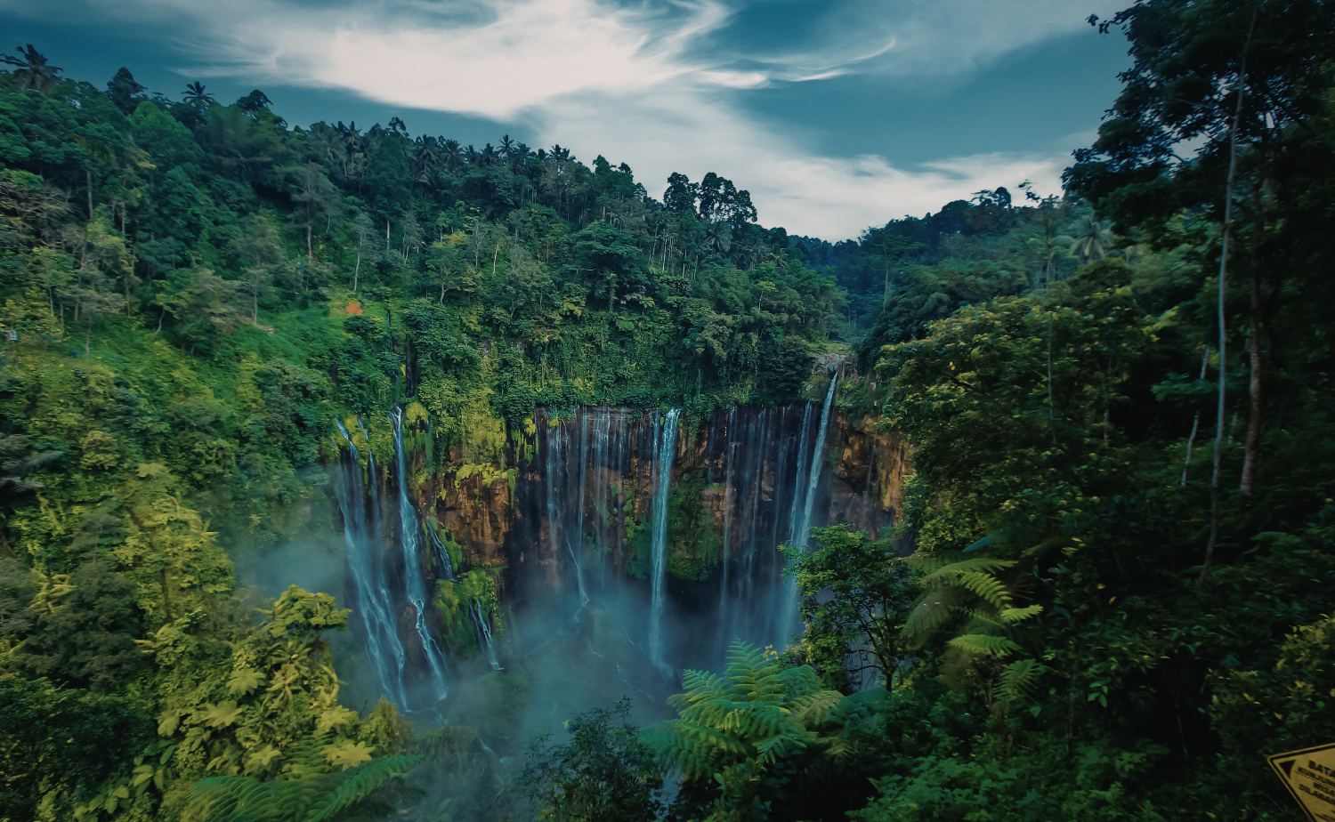 Tall waterfall cascading into a misty jungle basin surrounded by dense tropical greenery.