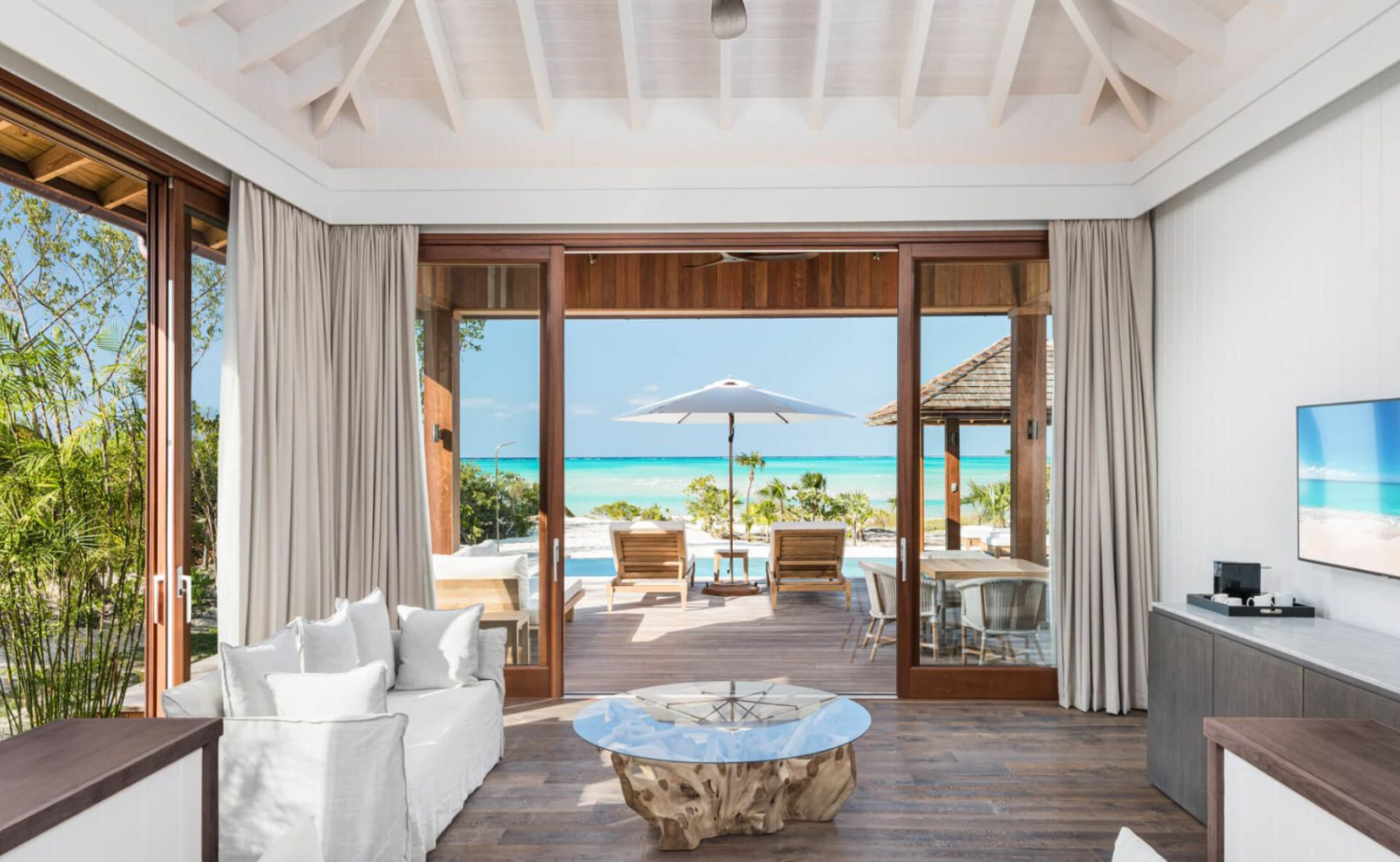 Bright luxury suite with sliding doors opening to a private terrace overlooking a Caribbean beach.