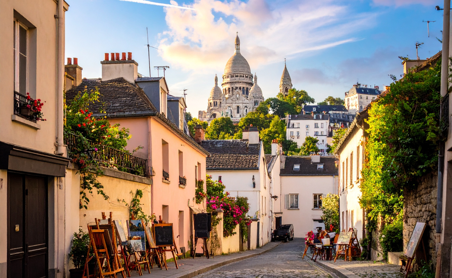 Charming Montmartre street lined with artists and cafés with Sacré-Cœur visible in the background.