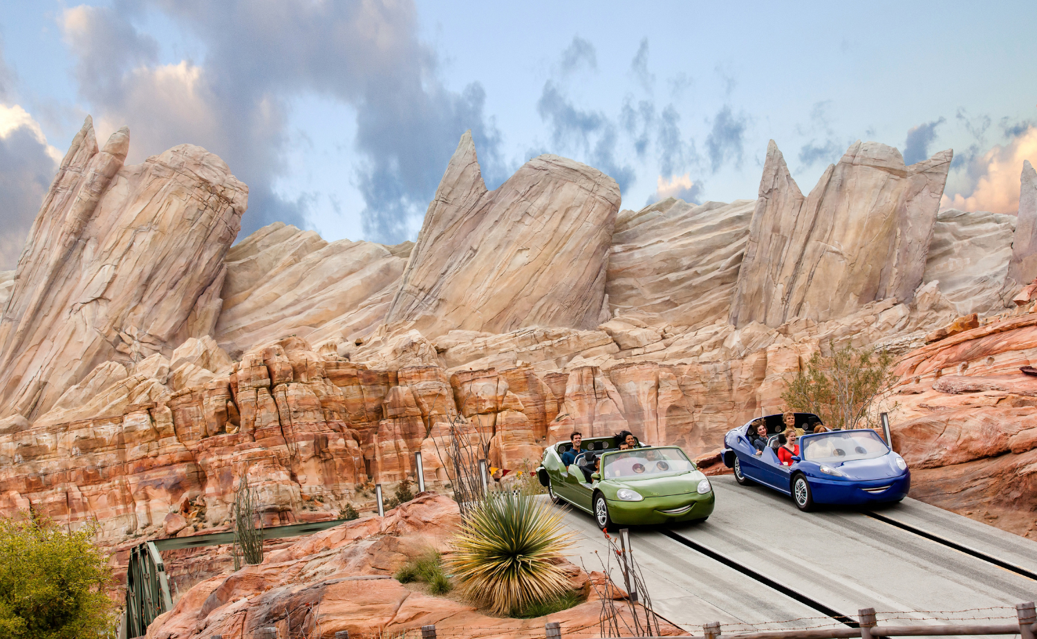 Green and blue race cars traveling through the desert landscape on Radiator Springs Racers at Disney California Adventure Park.