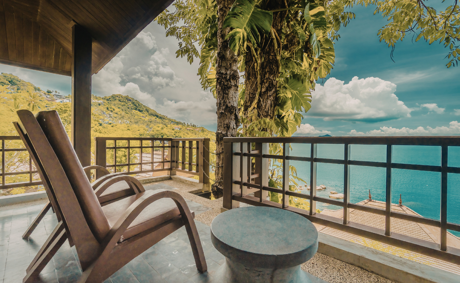 Ocean view from a tropical balcony with lounge chairs overlooking lush hillsides and calm blue water, illustrating the peaceful pace of a Pacific island escape.