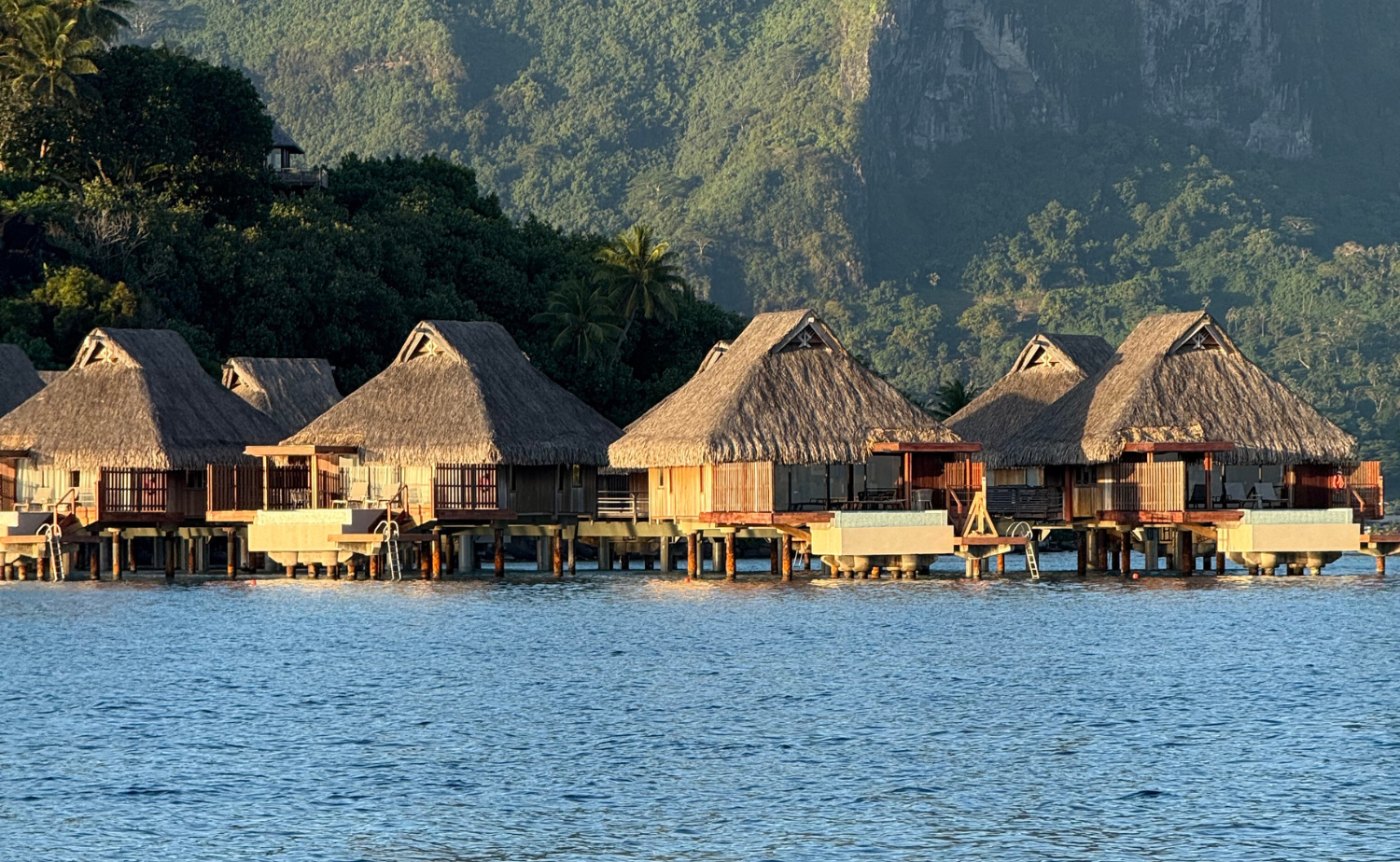 Overwater bungalows in Tahiti set above calm lagoon waters with lush mountains behind, representing a luxury and secluded island stay.