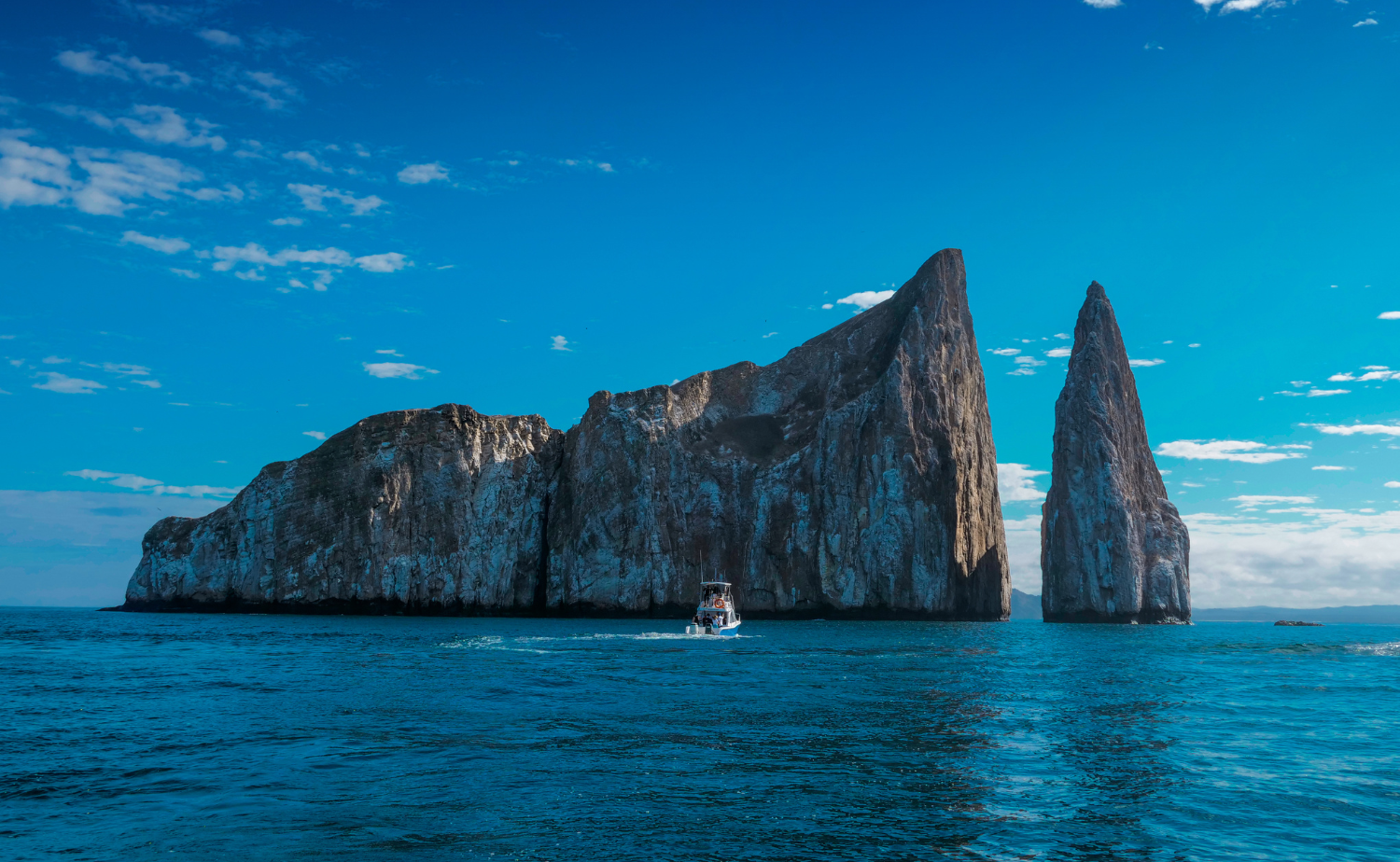 Small boat cruising past the dramatic volcanic formations of Kicker Rock in the Galápagos Islands.