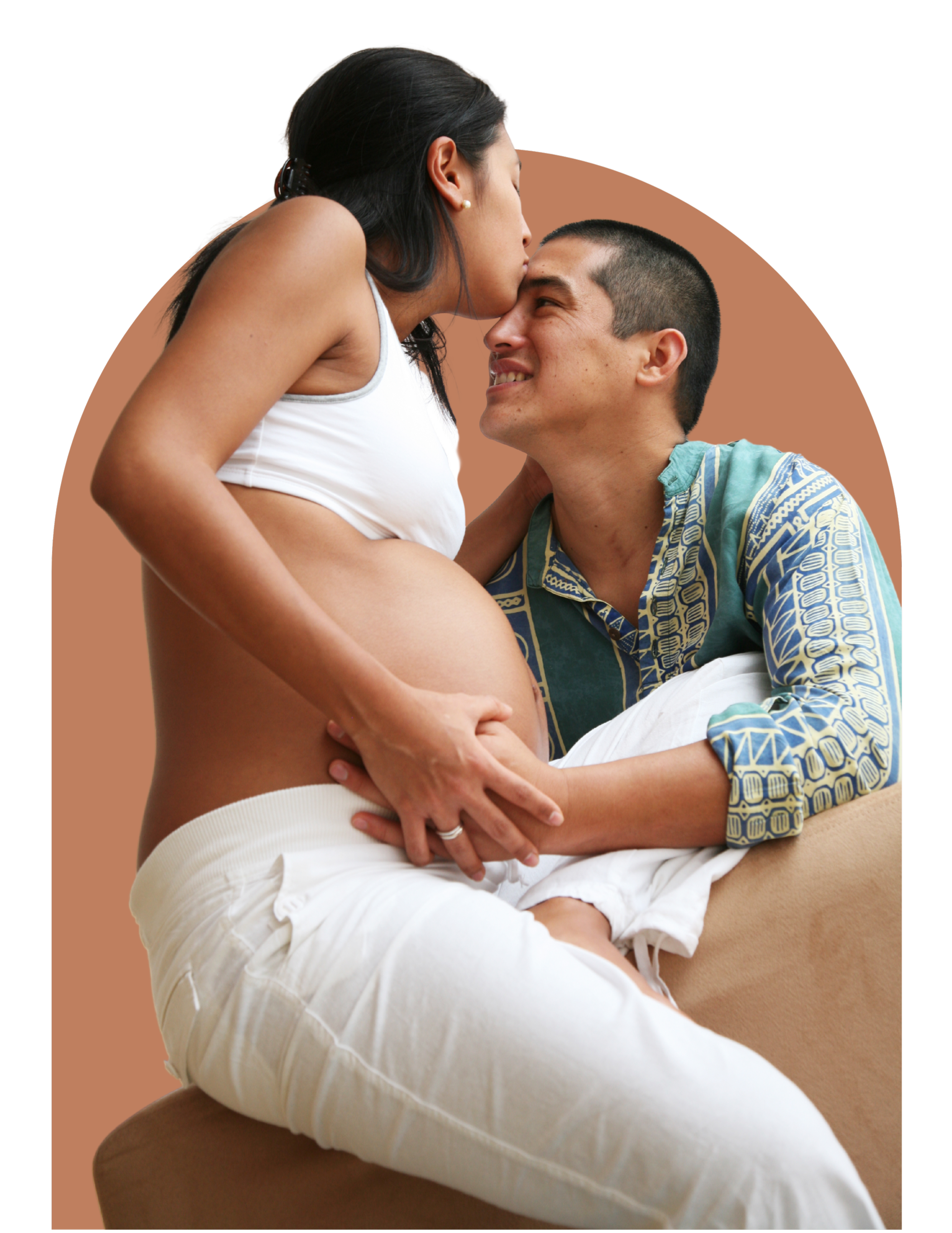 A pregnant woman sits sideways on her partner's lap, kissing his forehead. They are holding hands over her pregnant belly.