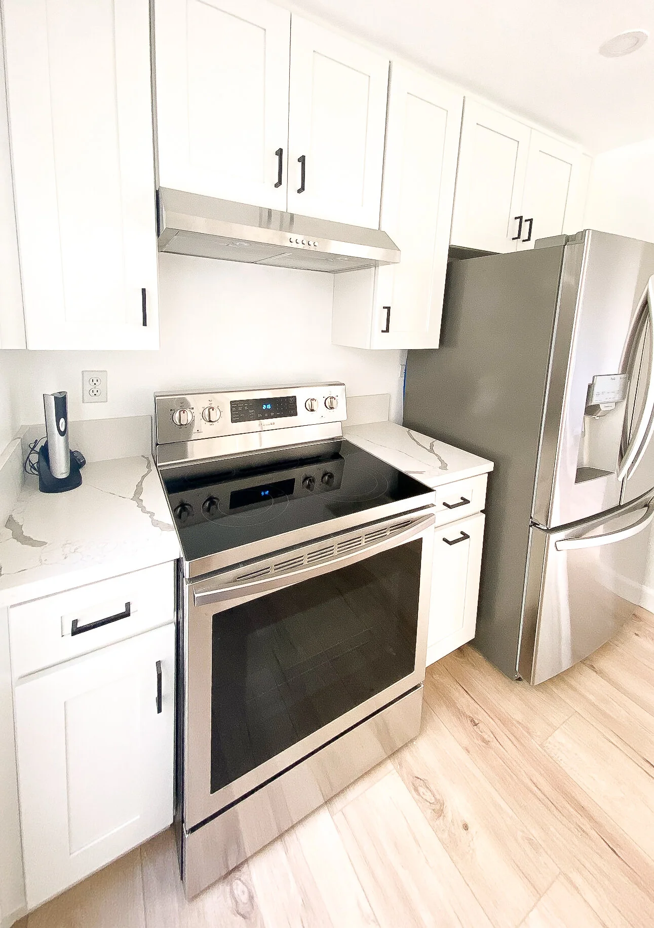 Modern kitchen with white cabinets, a stainless steel oven and stove, a stainless steel refrigerator with a water dispenser, and a marble countertop.