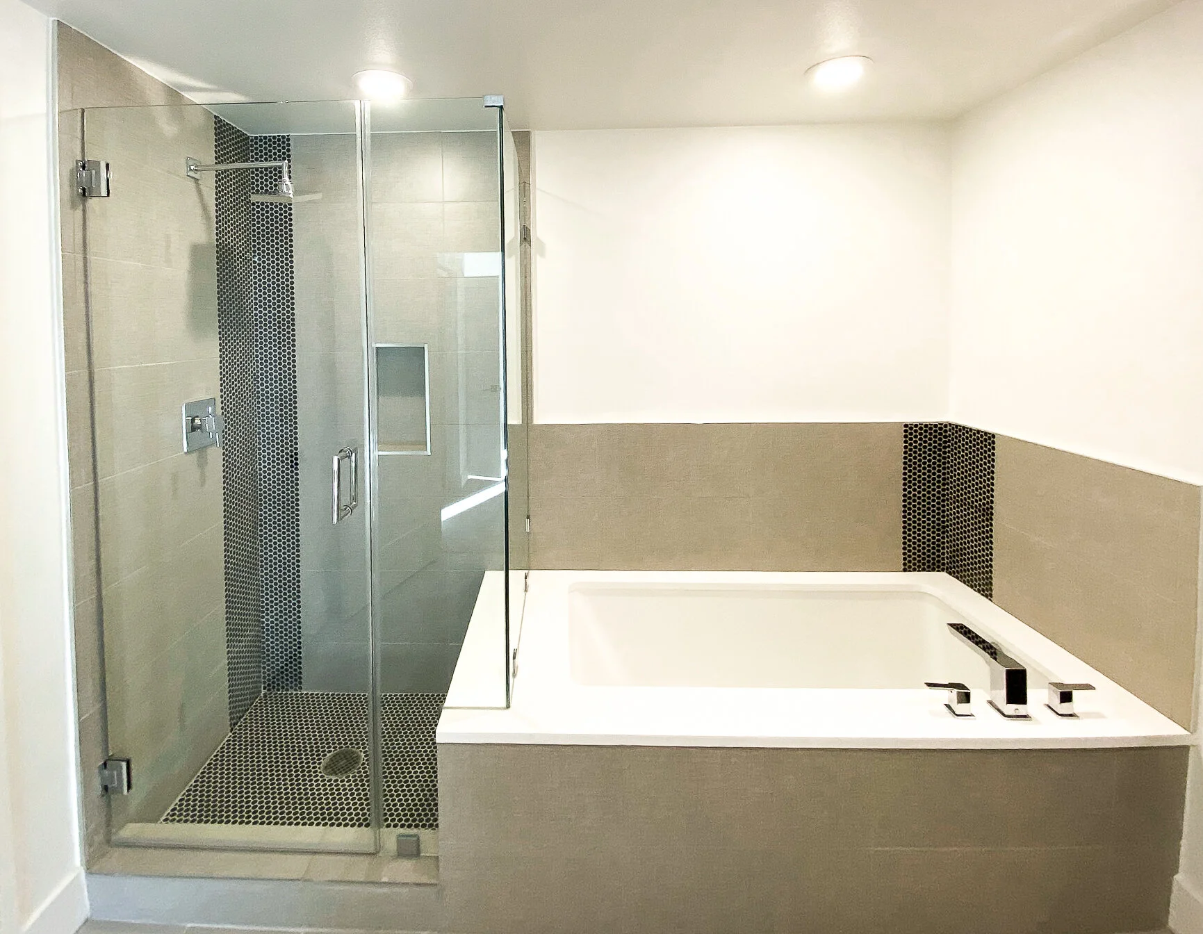 Modern bathroom with a glass-enclosed shower and built-in bathtub, featuring black hexagonal tiles and beige wall tiles.