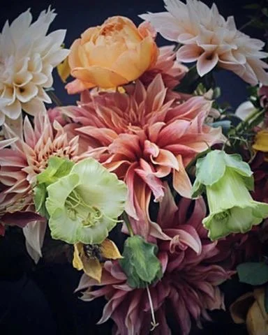 A bouquet of various large, colourful flowers including dahlias in shades of peach, cream, and green.