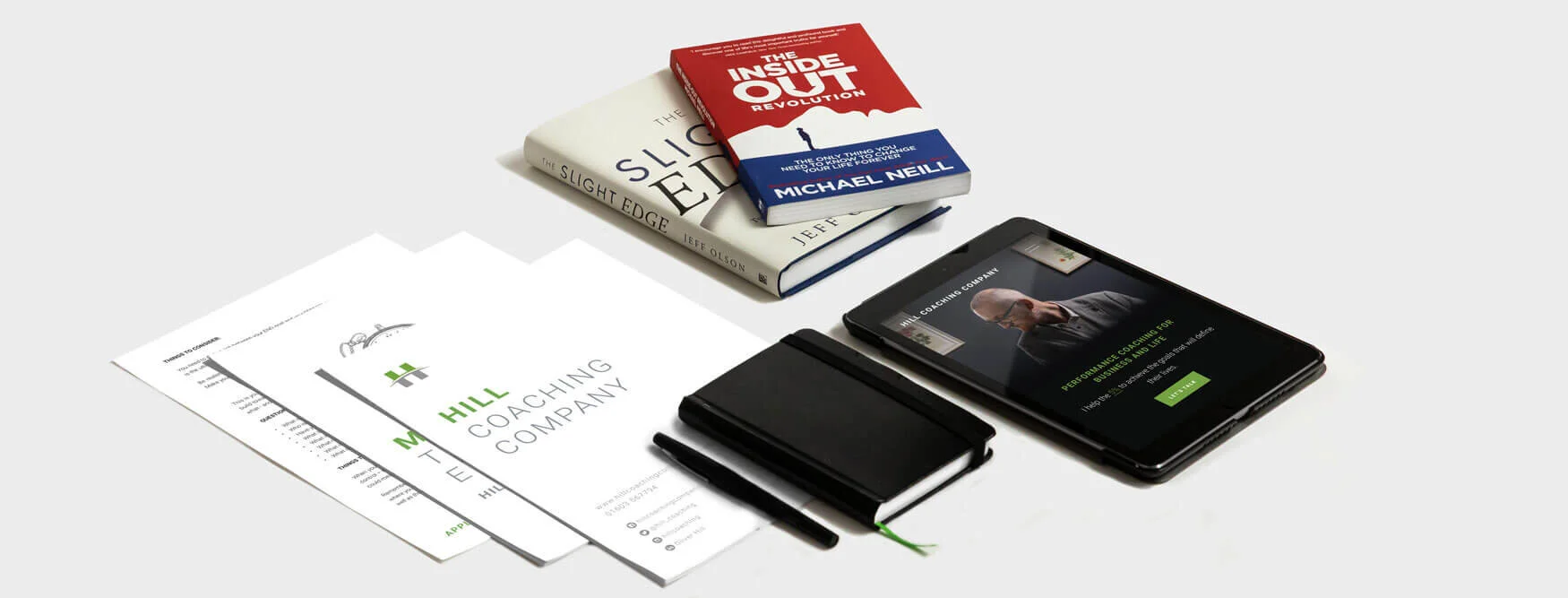 Photograph of personal development books, guides, an iPad featuring the Hill Coaching Company website and a notebook.