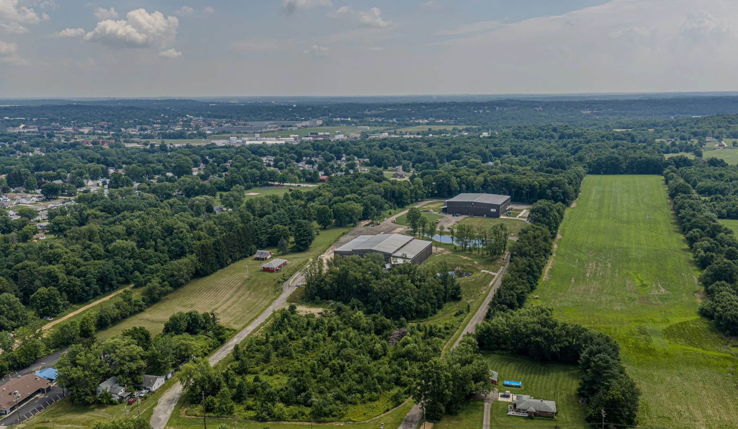 Aerial view of KDA's Norton, Ohio industrial park, showing two manufacturing buildings, access roads, wooded surroundings, and adjacent land for future development.
