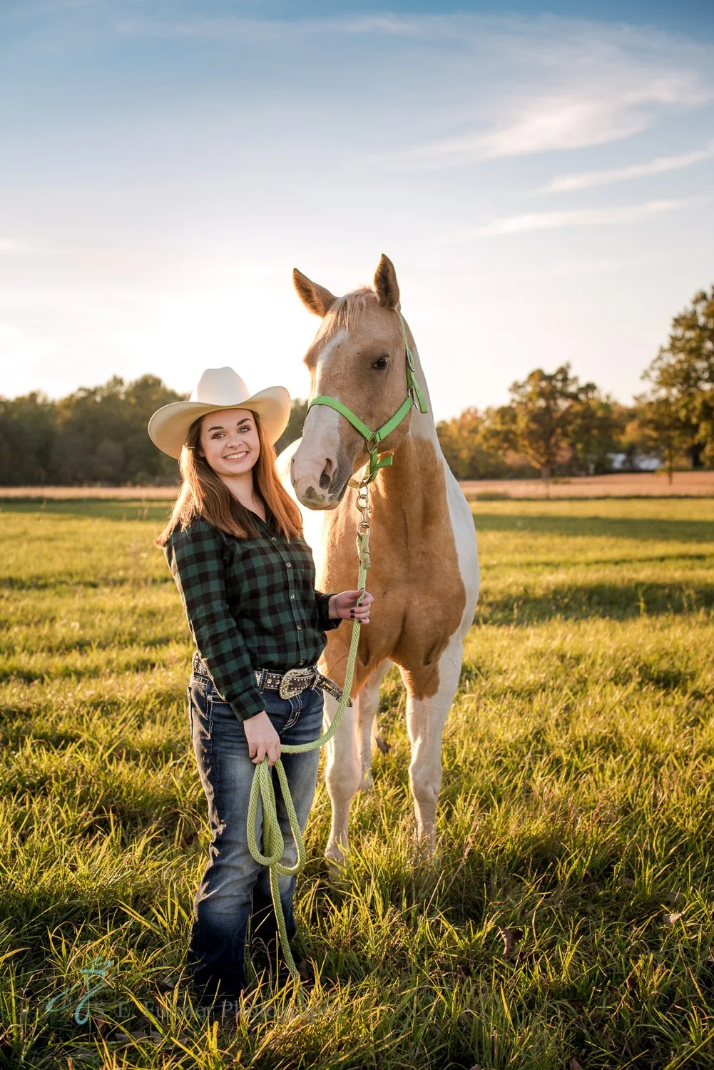 High school senior, Goodrich, MI. Woman in a cowboy hat standing with a horse in a grassy field at sunset. North Branch, MI