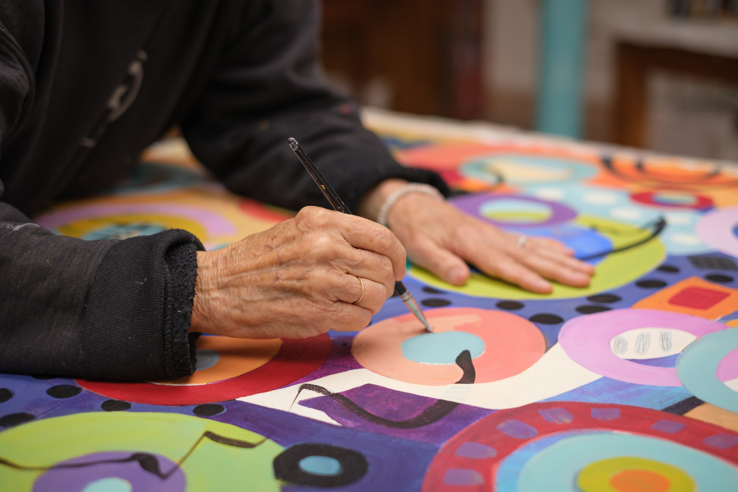 Person painting a colorful abstract artwork with circles and geometric shapes.