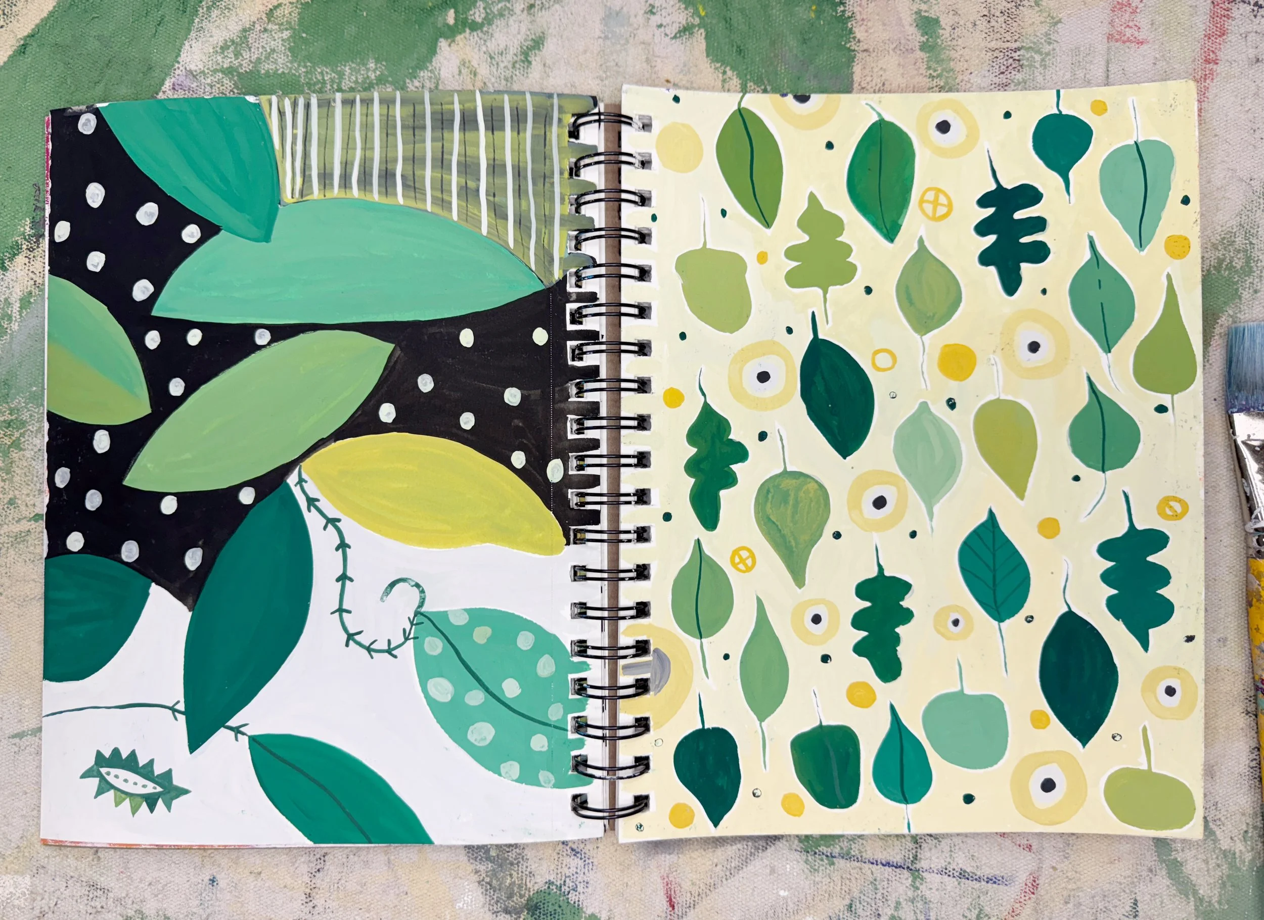 Open sketchbook with abstract leaf designs, leaves in various shades of green and yellow on both pages, on a colorful, textured background.