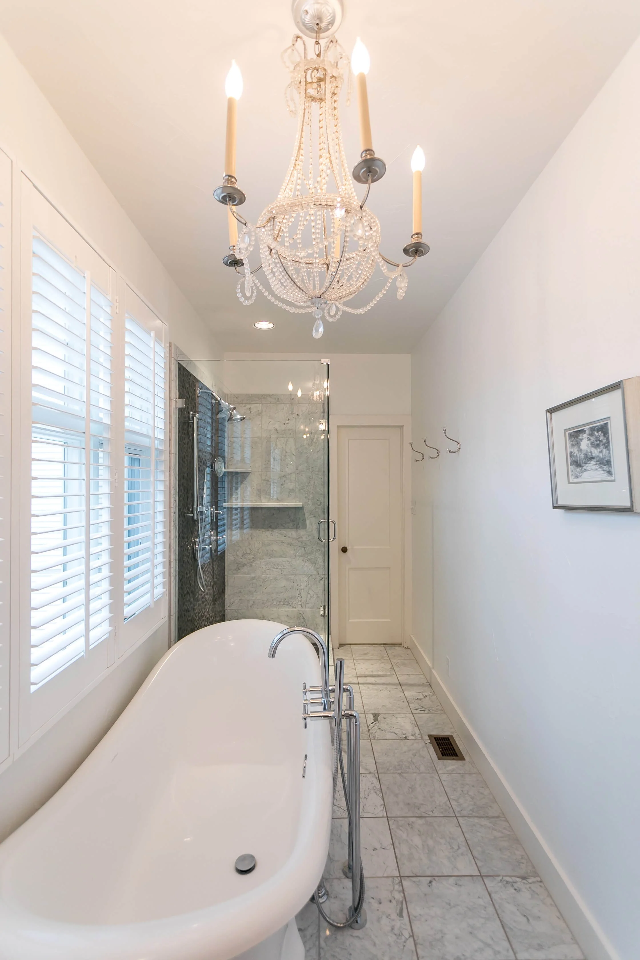 White window shutters providing light and privacy beside a freestanding tub in Fredericksburg, Texas