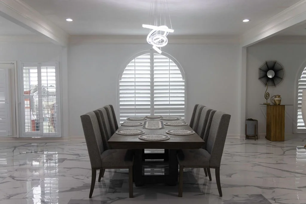 Modern dining room in urban Dallas home featuring Rockwood Shutters on an arched window.