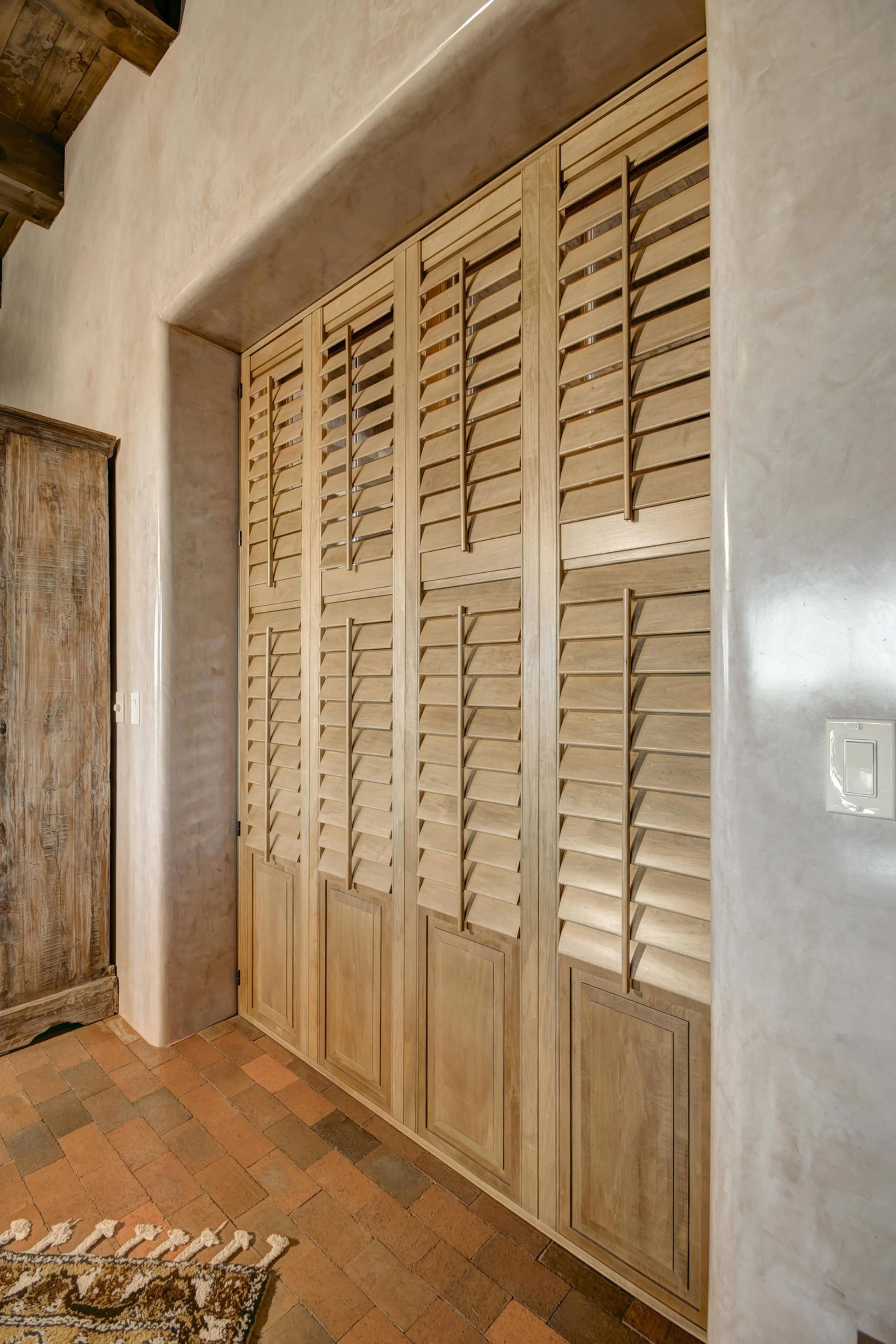 Southwestern Santa Fe living room with Sands-stained hardwood shutters, exposed wood beams and plaster doorways.