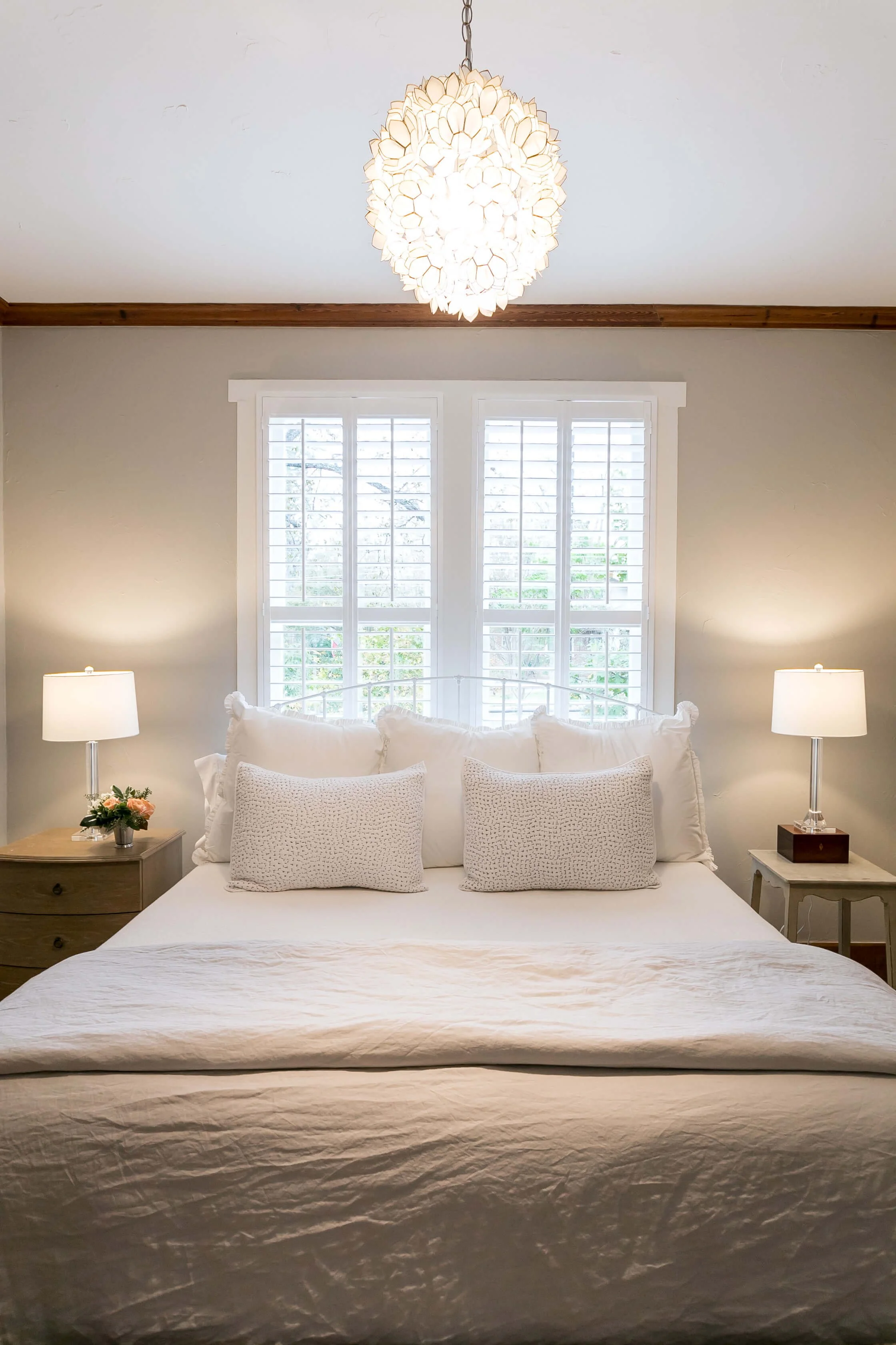 White plantation shutters behind a guest bed in the historic-style Bella Regalo vacation rental in Fredericksburg, Texas