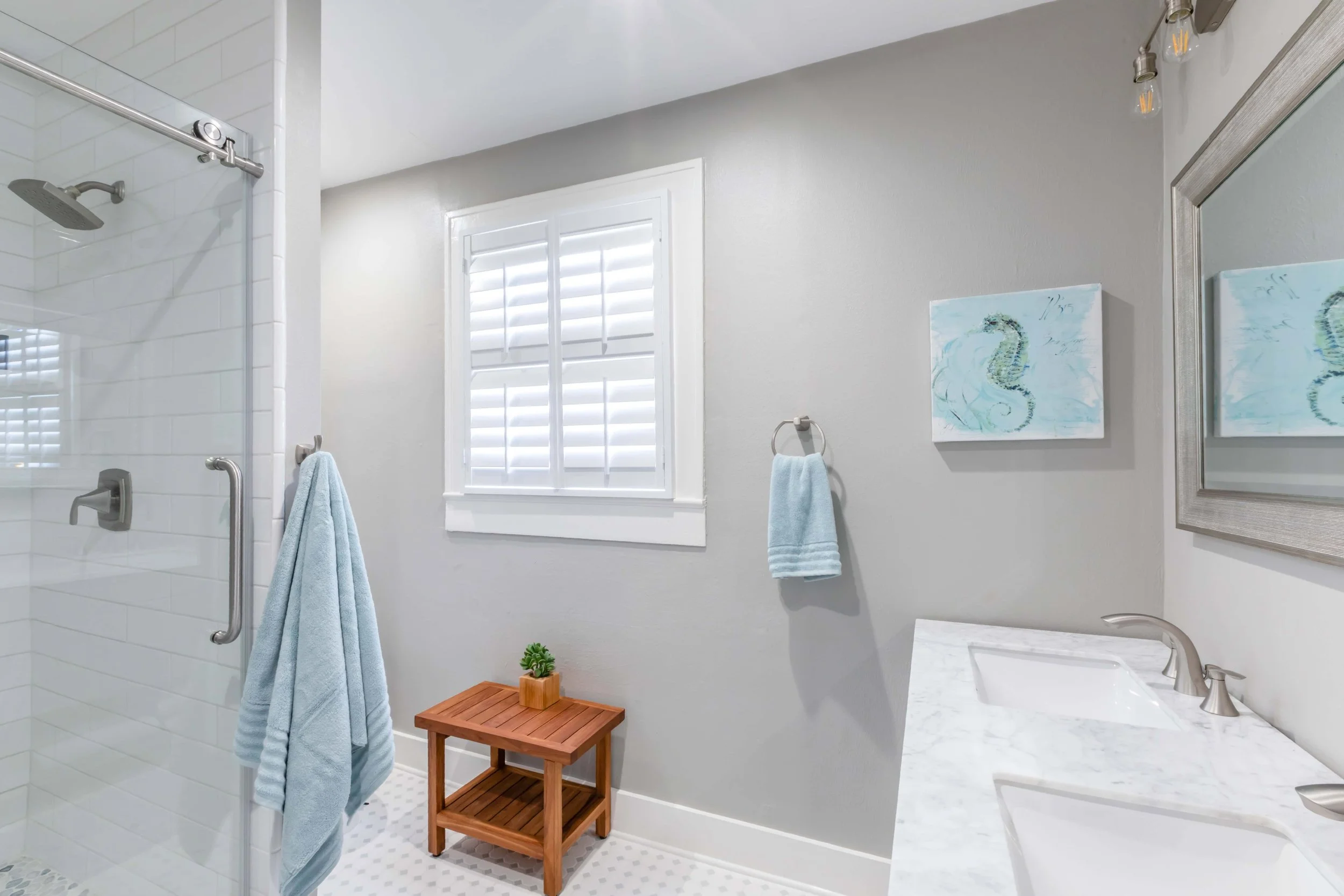 Coastal bathroom with white plantation shutters, blue accents and a marble vanity in Galveston, TX.