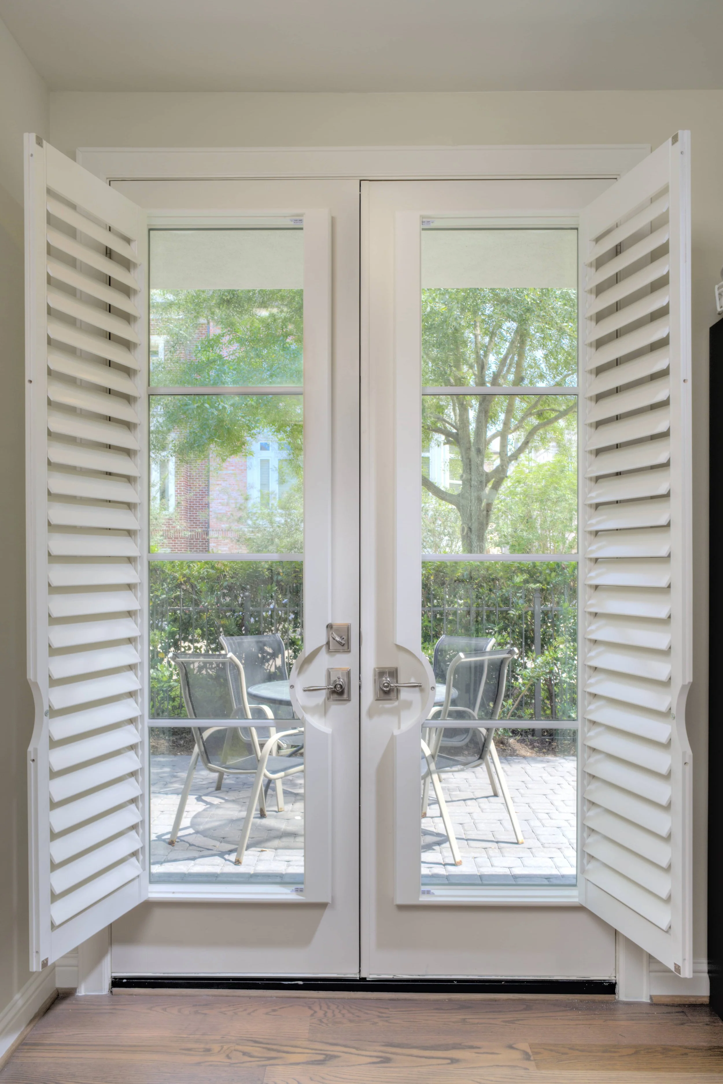 Custom French door shutters shown open around the glass doors of a The Woodlands, Texas home.
