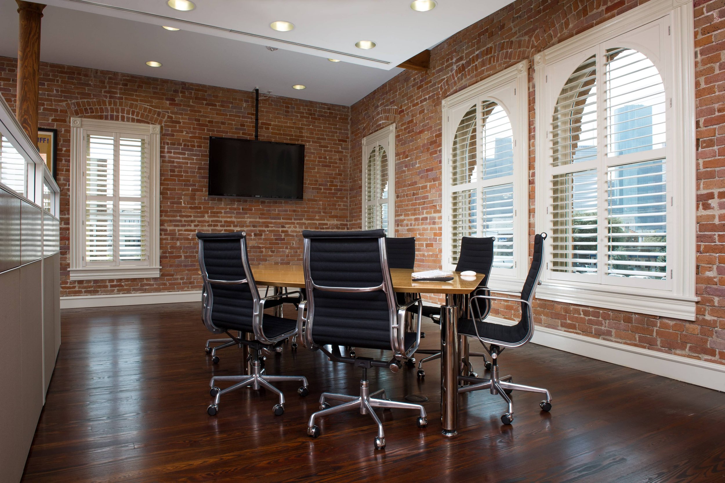 Custom white shutters follow specialty arched windows in a brick St. Louis firehouse meeting room.