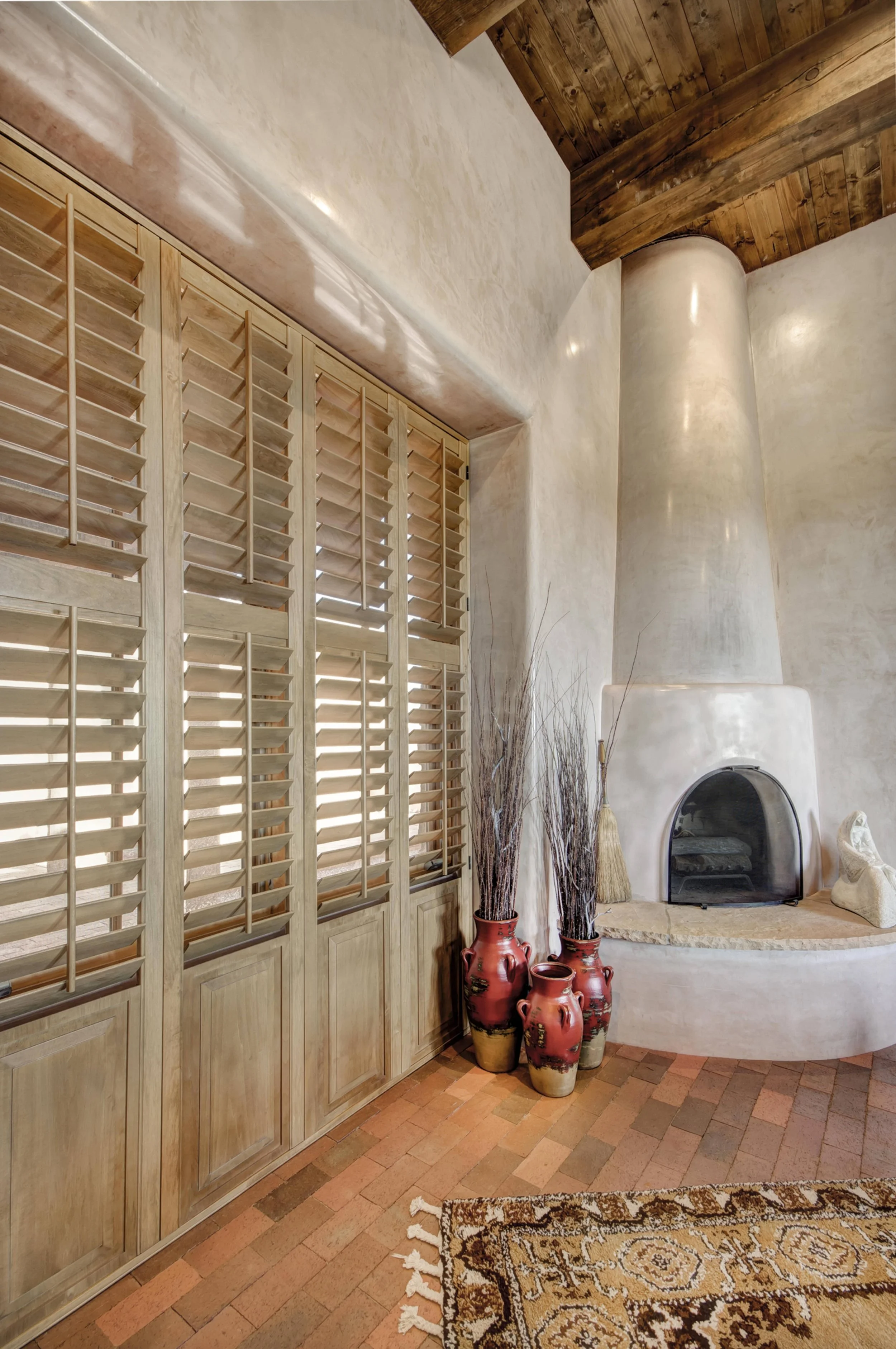 Sands-stained hardwood shutters complement plaster walls, wood ceiling beams and a kiva fireplace in a Santa Fe home.