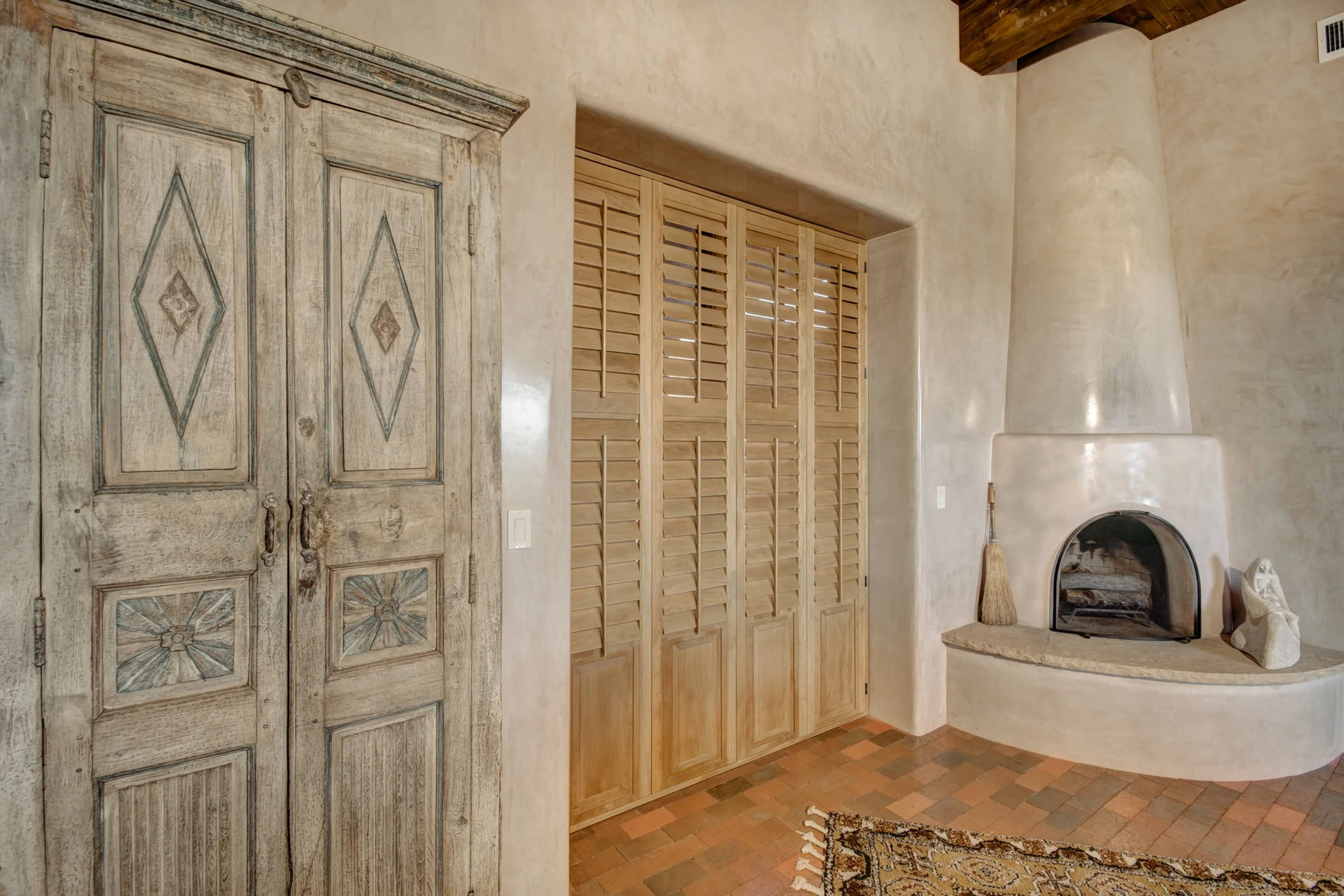 Sands-stained hardwood shutters and a traditional kiva fireplace in a Southwestern Santa Fe interior.