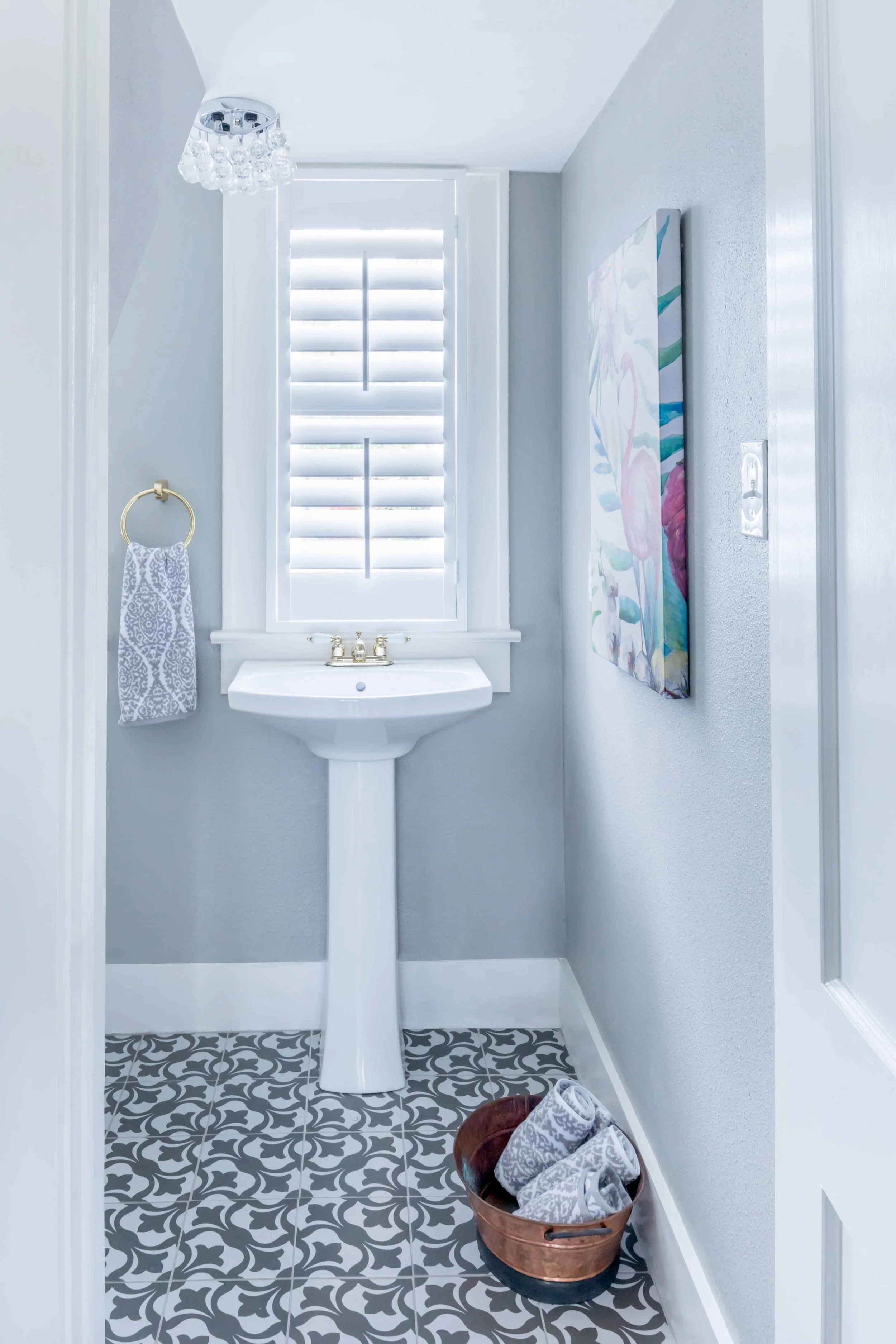 White plantation shutters above a pedestal sink in a small Galveston beach house powder room.