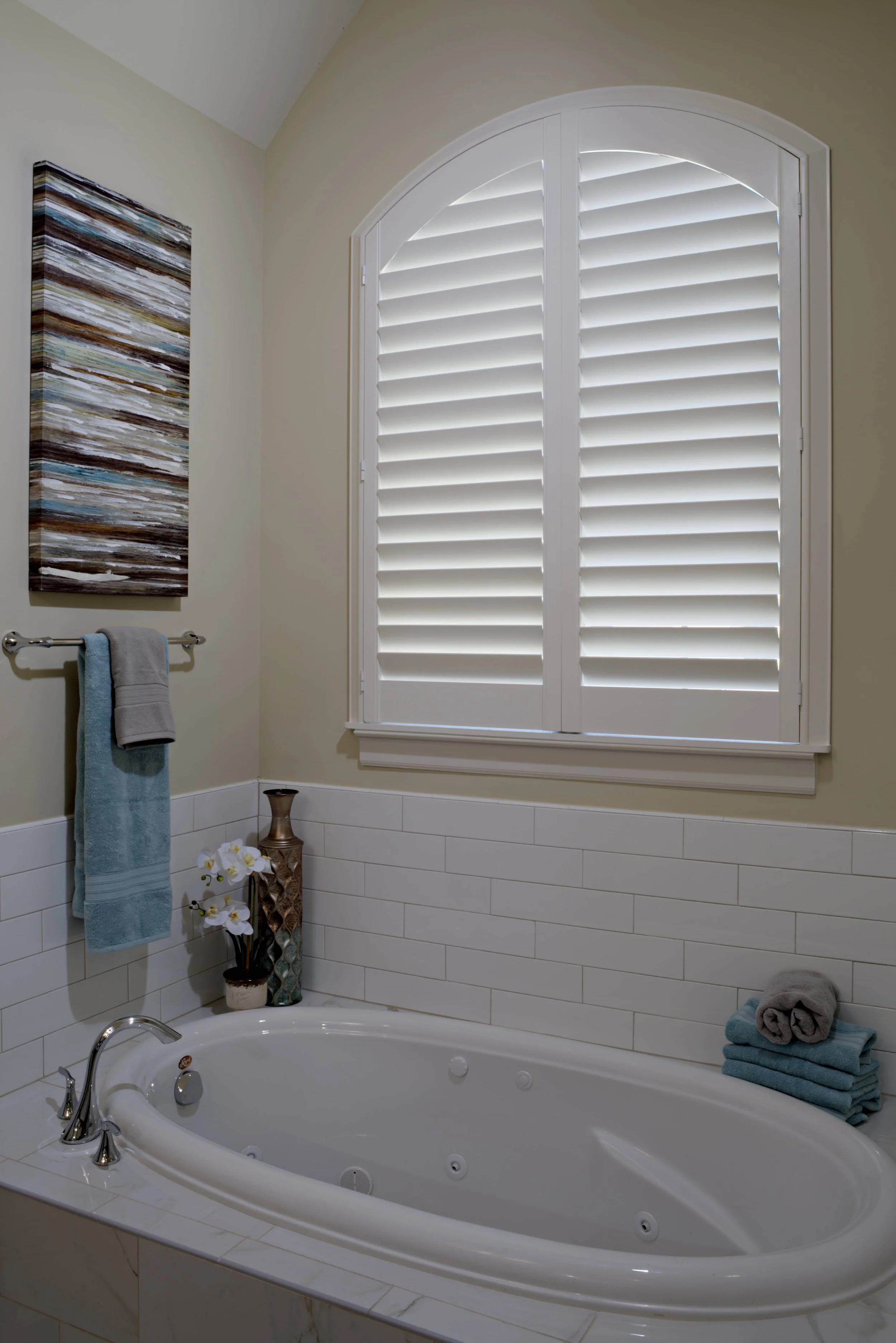 Custom white arched ClearLine shutter above a bathtub in a The Woodlands, Texas bathroom.