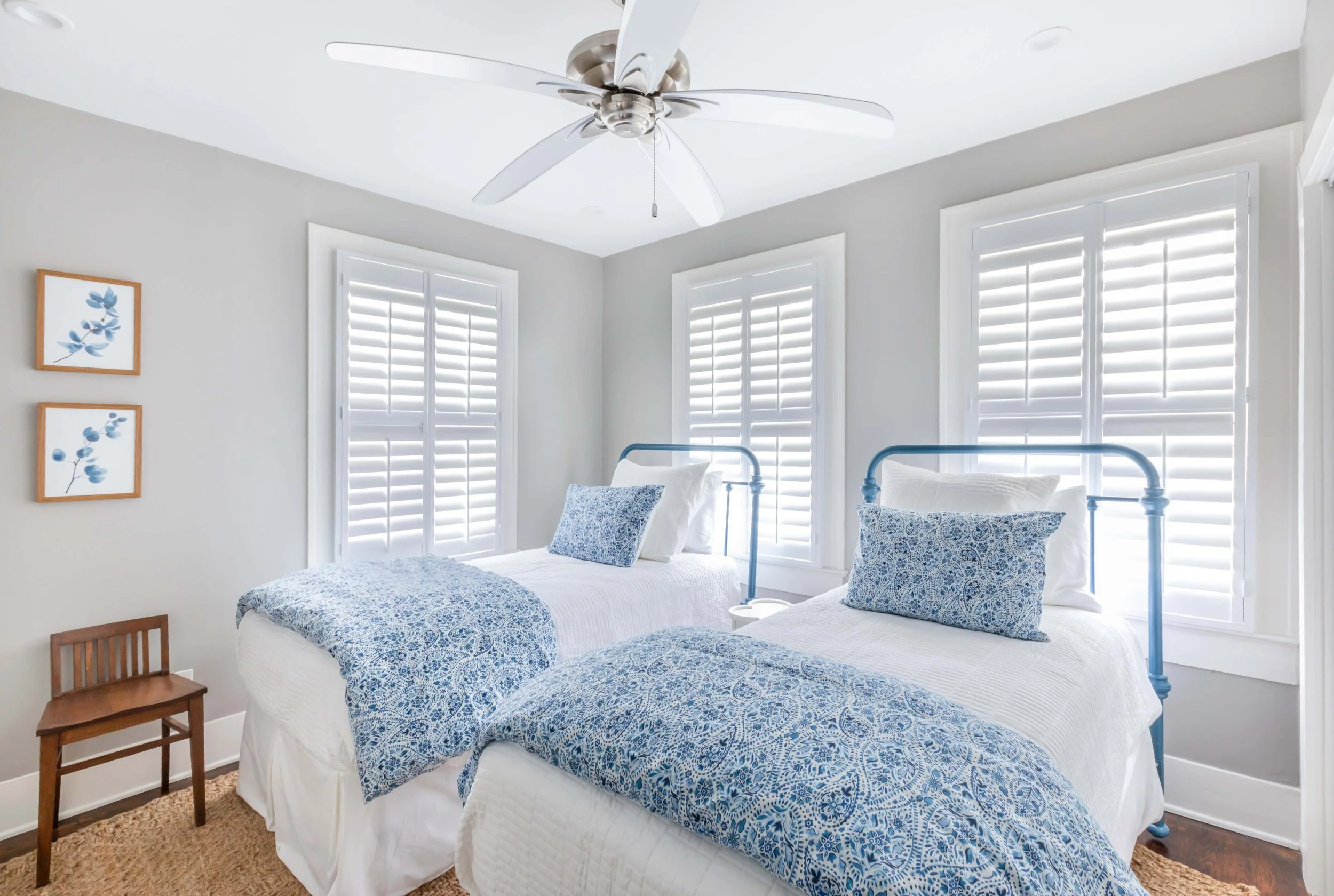 Twin bedroom with white plantation shutters and blue coastal bedding in a Galveston beach house.