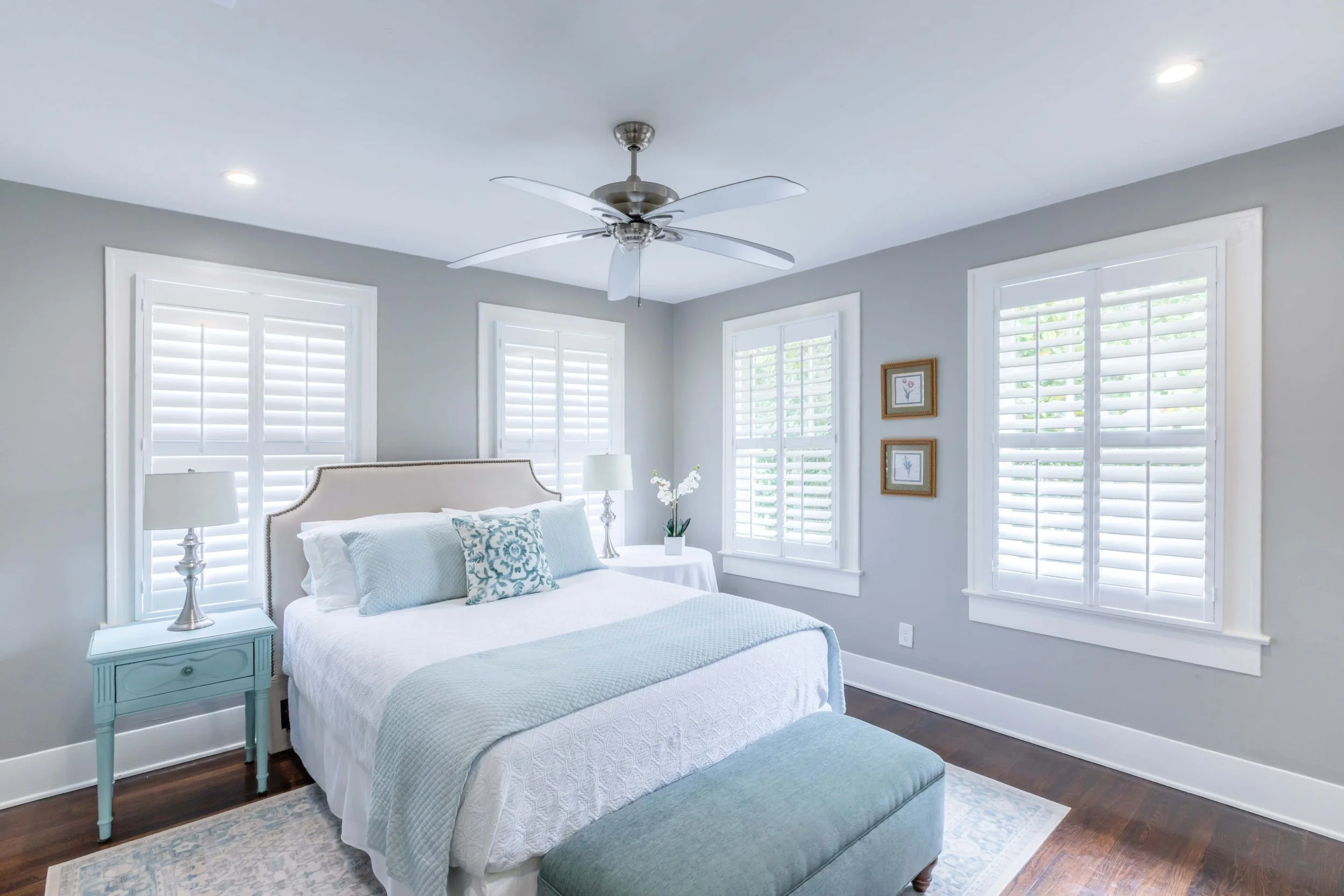 Coastal bedroom with white plantation shutters, soft blue accents and hardwood floors in Galveston, TX.