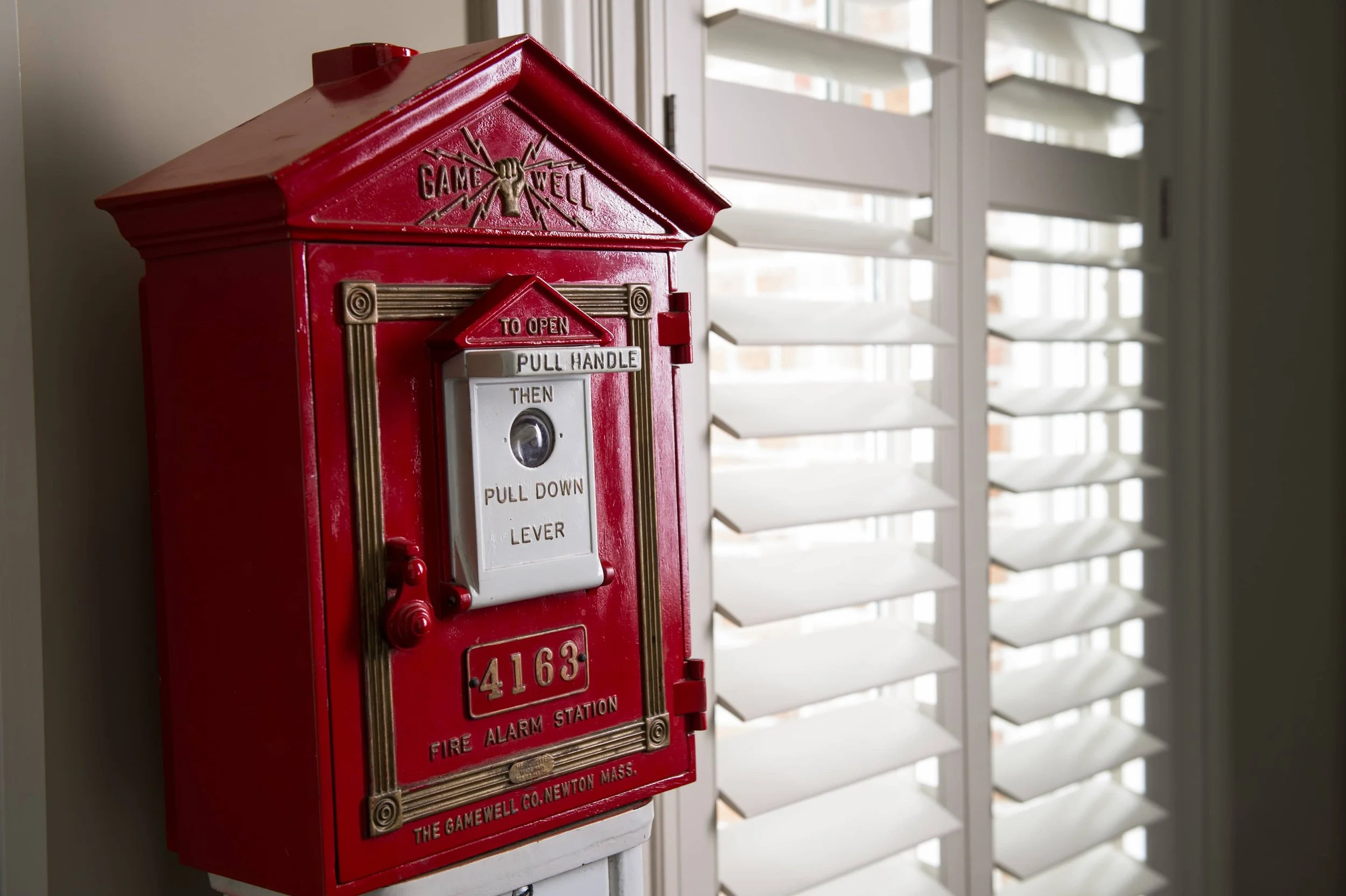 Custom white shutters beside a vintage red fire alarm box in a St. Louis firehouse.