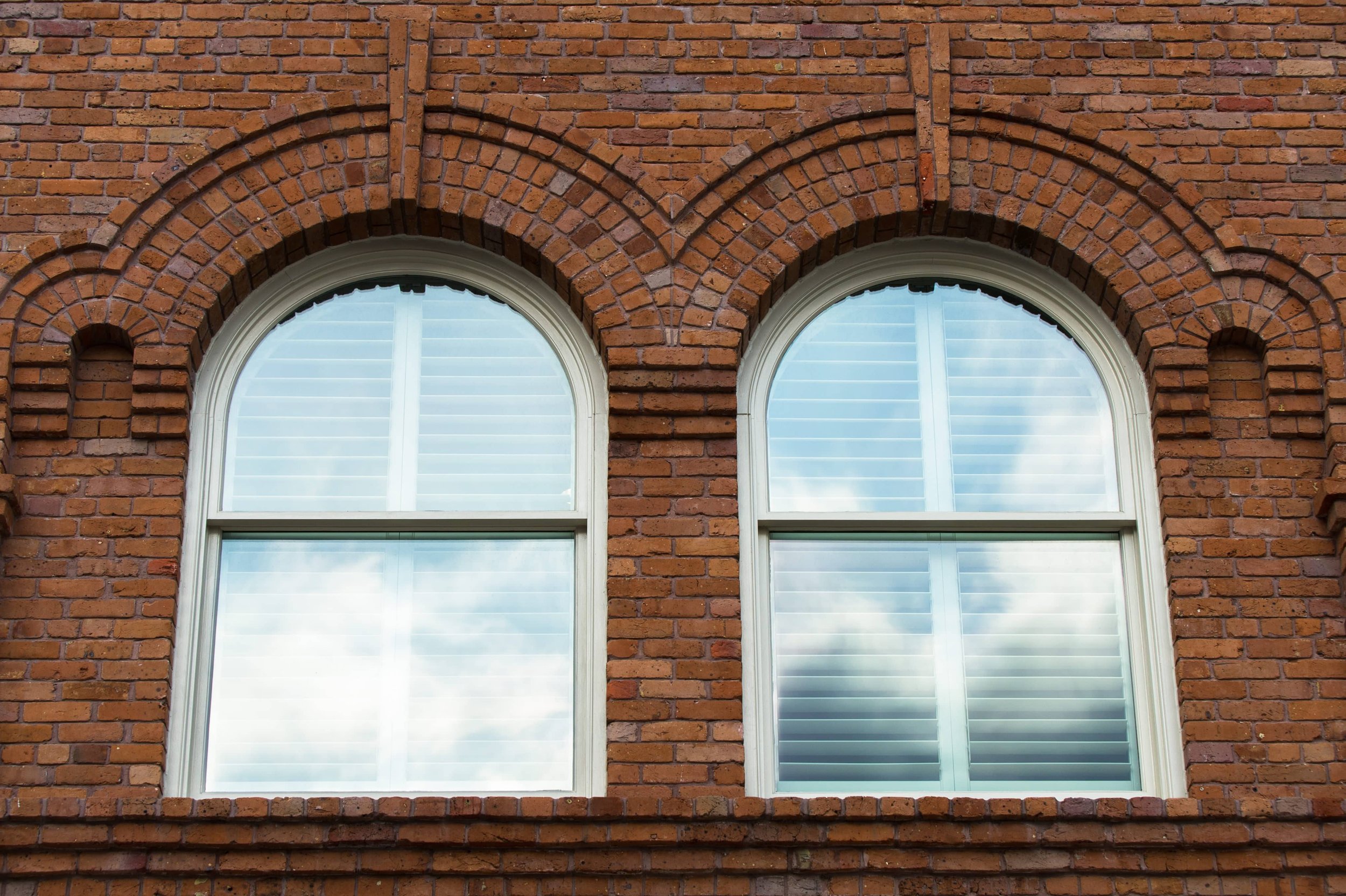 Custom shutters fitted to arched windows on a historic brick firehouse in St. Louis.