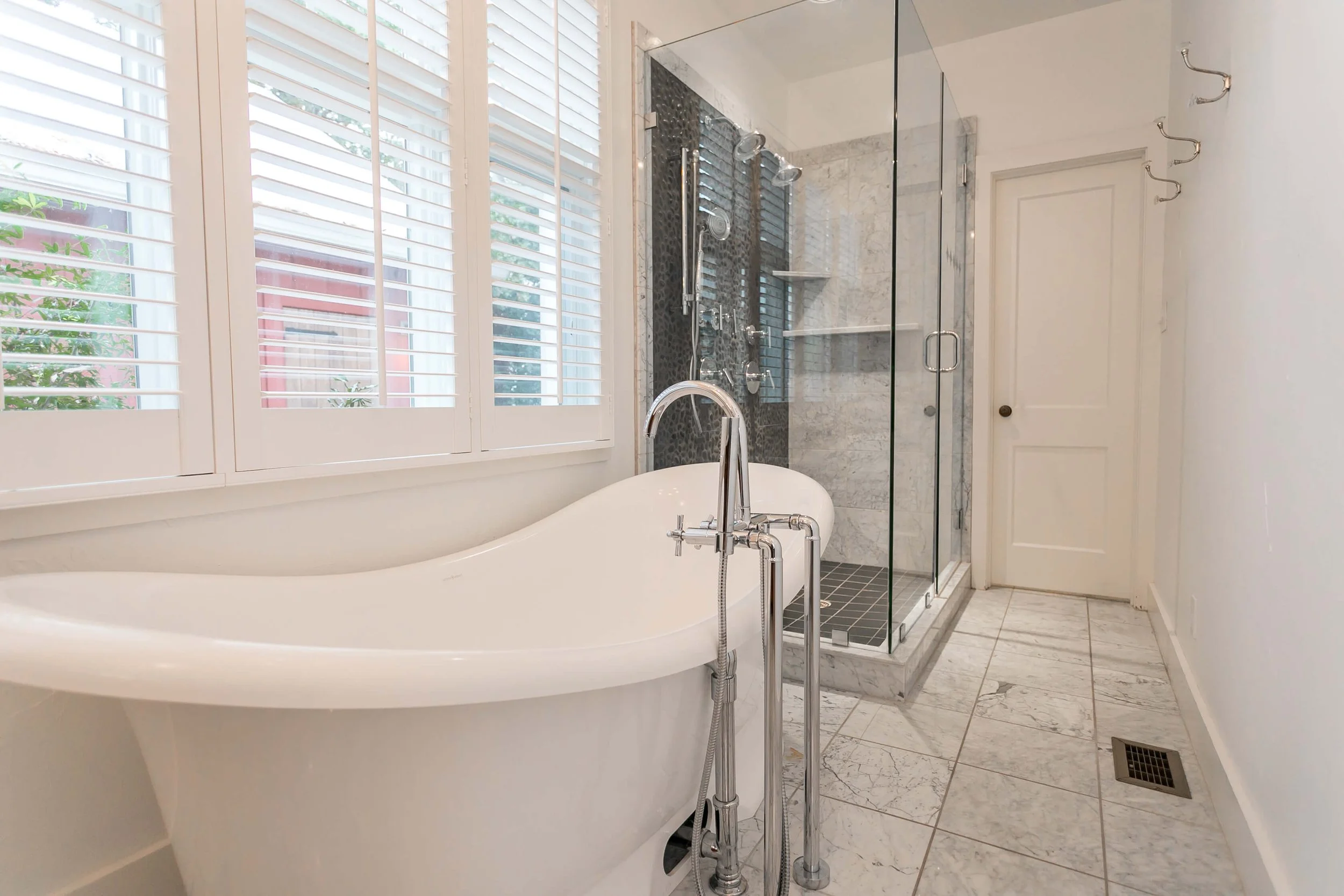 White plantation shutters beside a freestanding tub in a Fredericksburg, Texas vacation rental bathroom