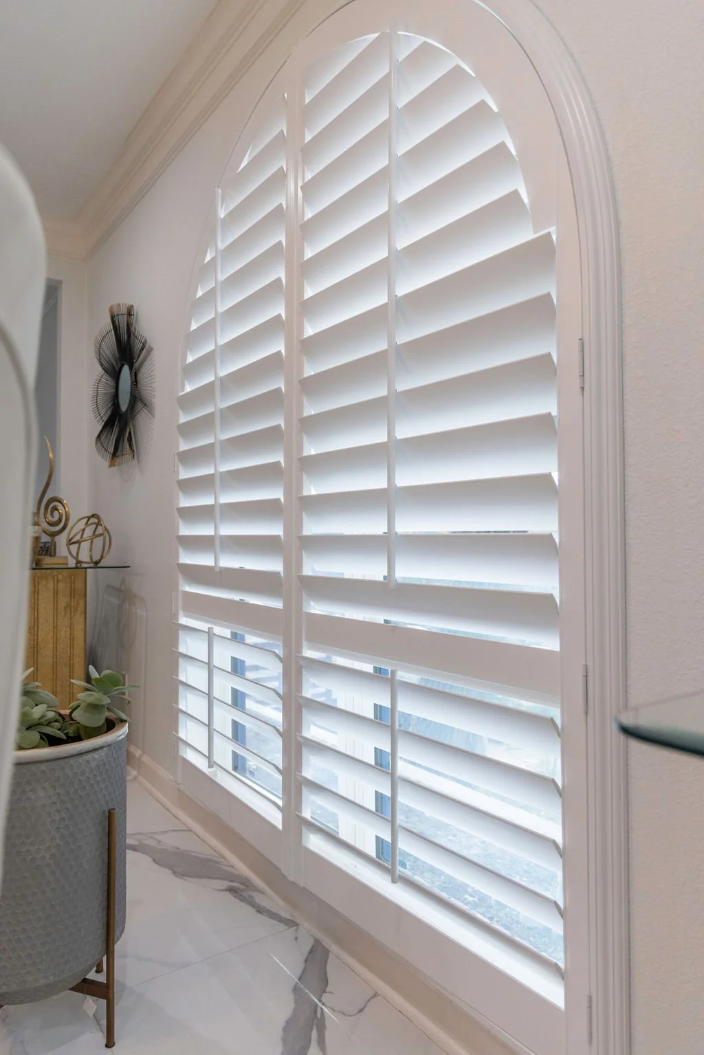 Close-up, angled photo of large arched window with Rockwood Shutters.  Wide panels with 4.5" louvers.