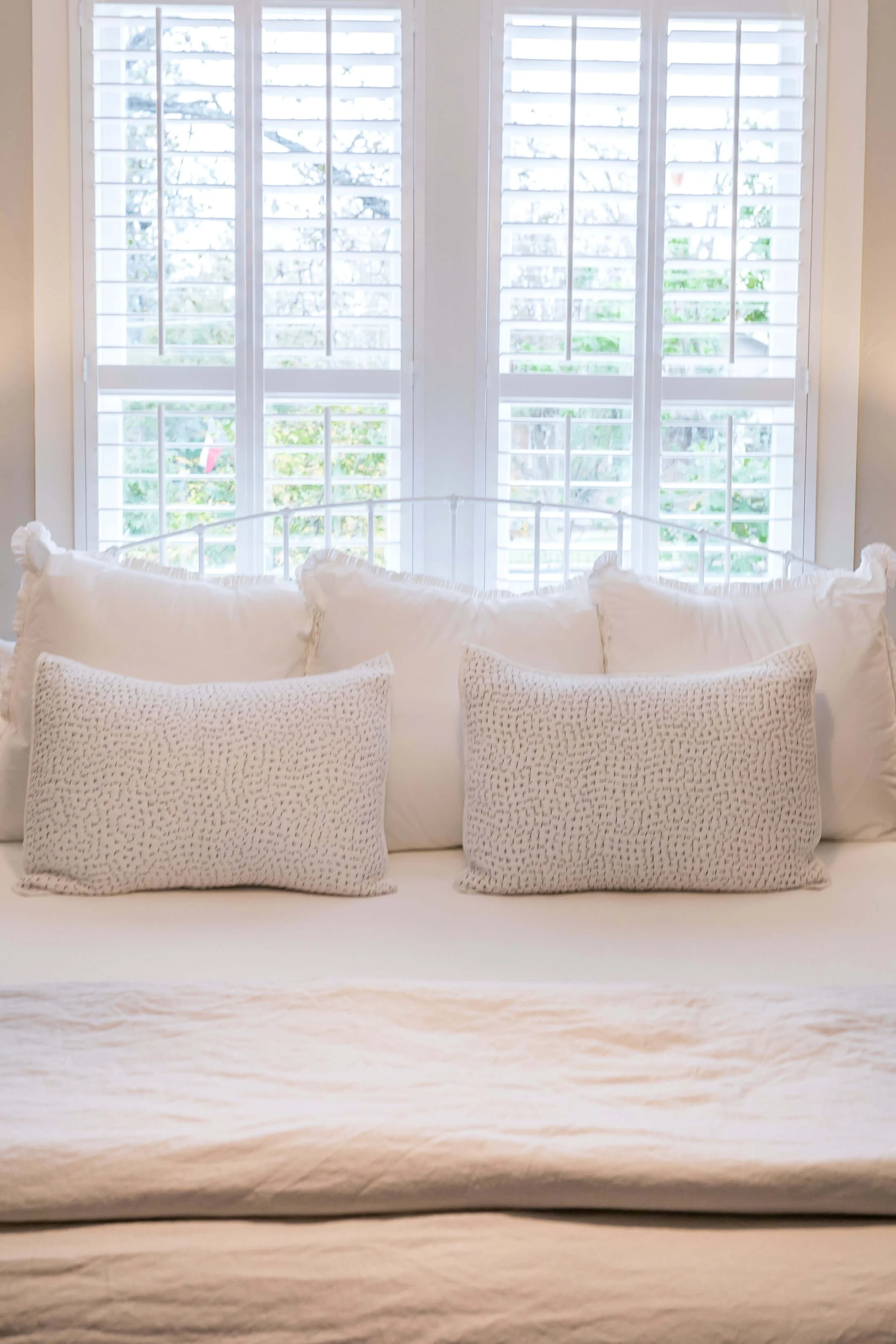 Close view of white plantation shutters above a guest bed at Bella Regalo in Fredericksburg, Texas
